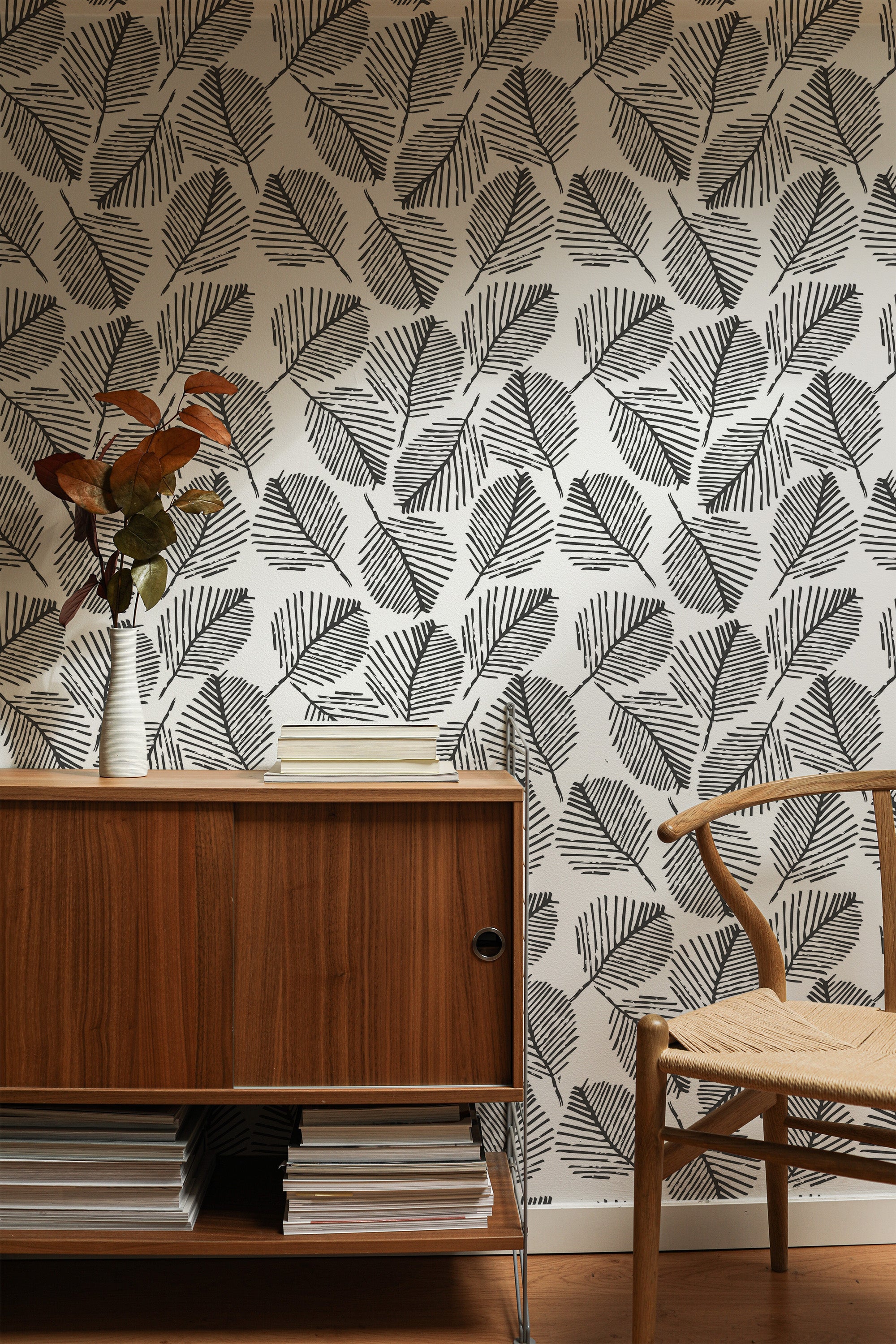 Self-adhesive wallpaper with a monochrome leaf stencil pattern on a room's wall, complemented by wooden furniture.