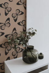 Self-adhesive Bold Butterfly wallpaper with large black and white butterfly patterns on a beige background, in a room with a green vase and plant on a white shelf.