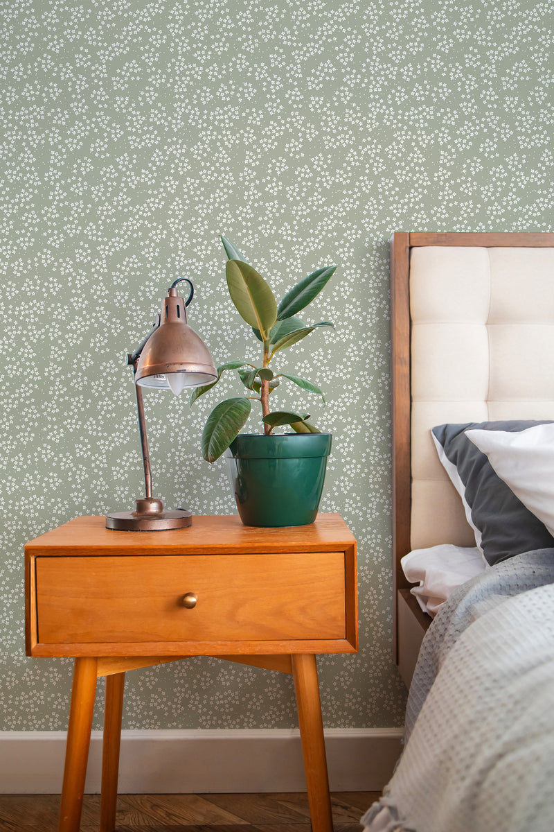 Self-adhesive wallpaper with a tiny floral pattern in a cozy bedroom, complementing a wooden bedside table, vintage lamp, and potted plant.