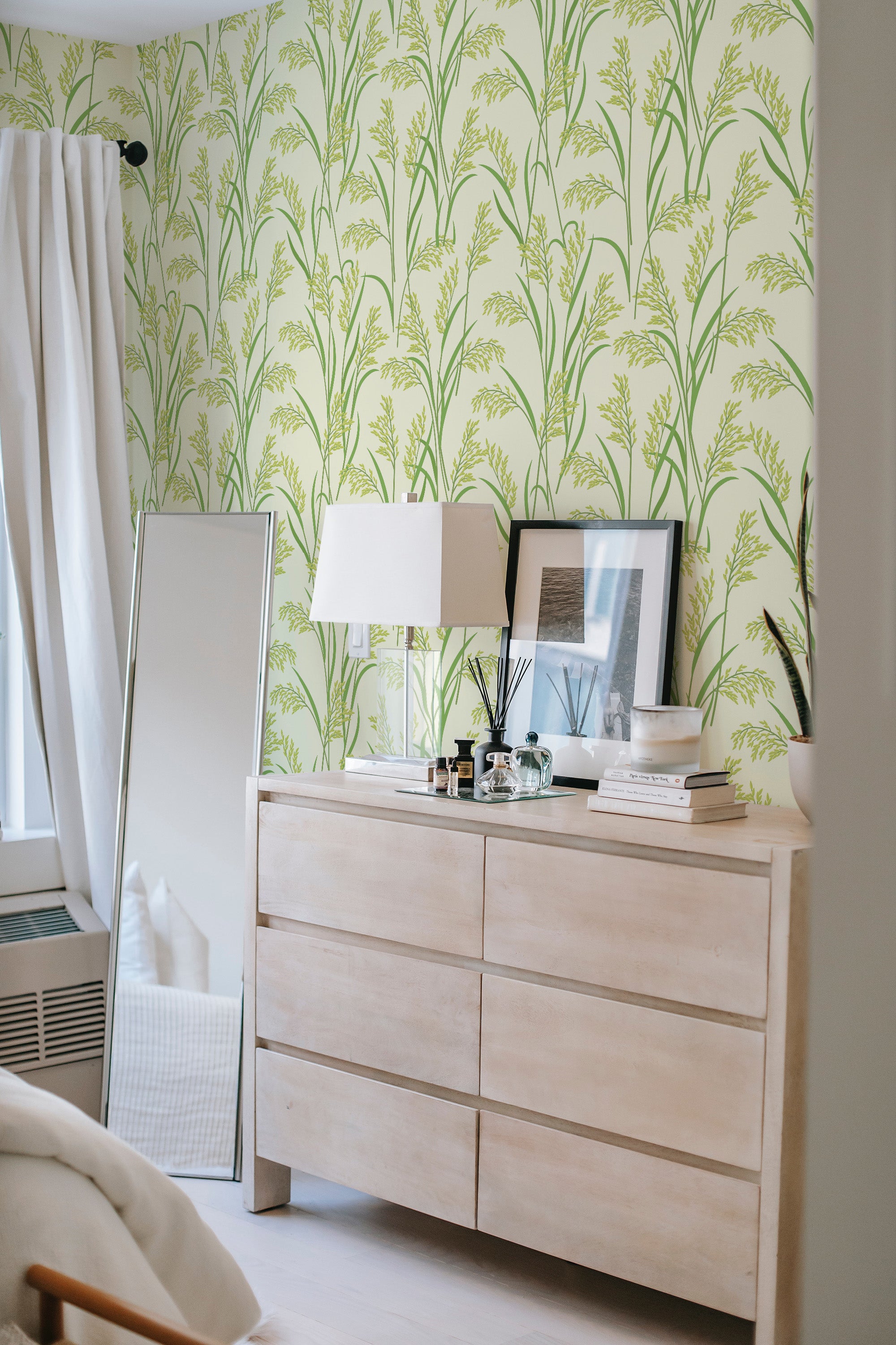 A light wooden dresser stands against a wall with green and yellow rice plant patterned wallpaper, giving a natural and calming aesthetic to the room. Traditional wallpaper.