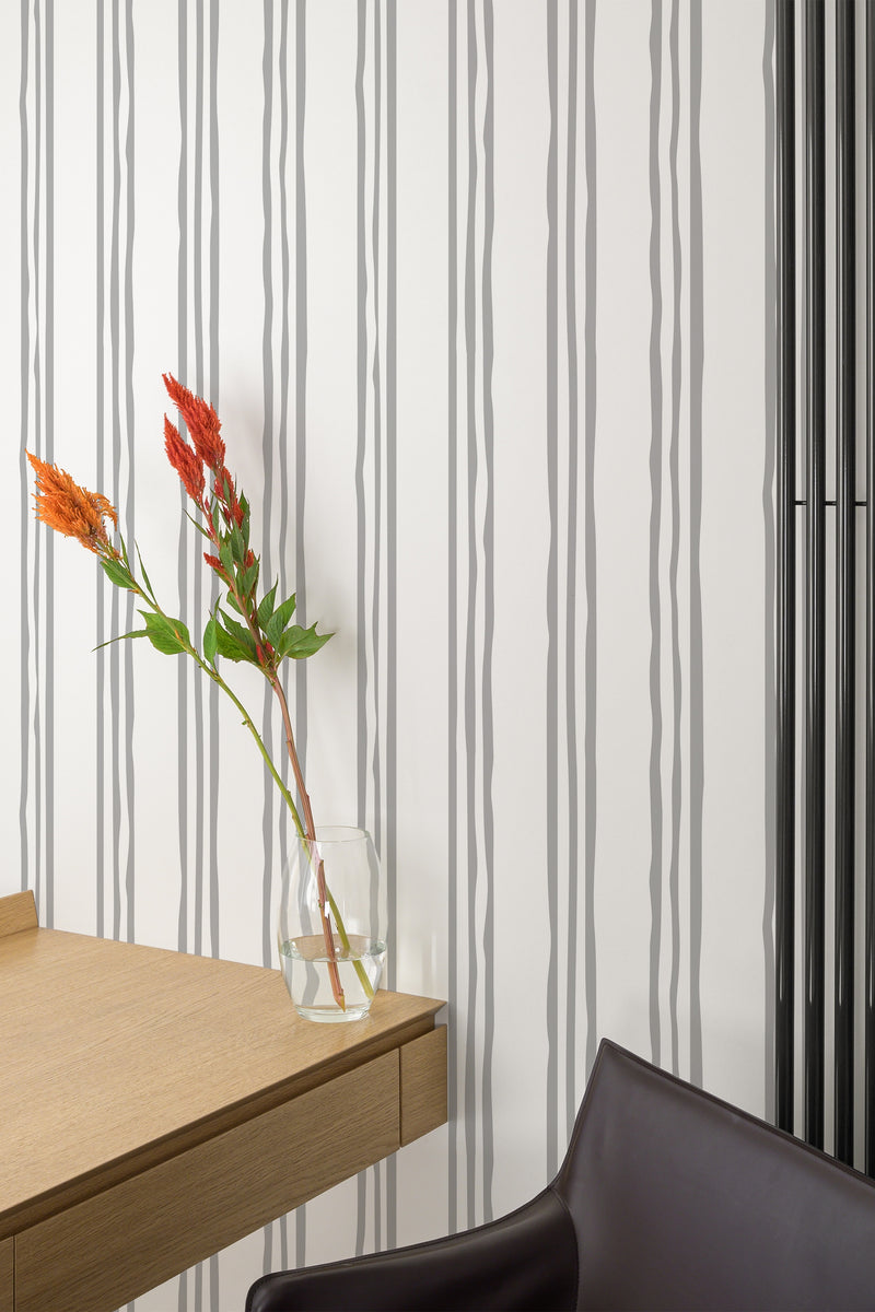 Self-adhesive wallpaper with vertical three-stripe pattern in alternating thicknesses on a wall in a room with minimalistic furniture.