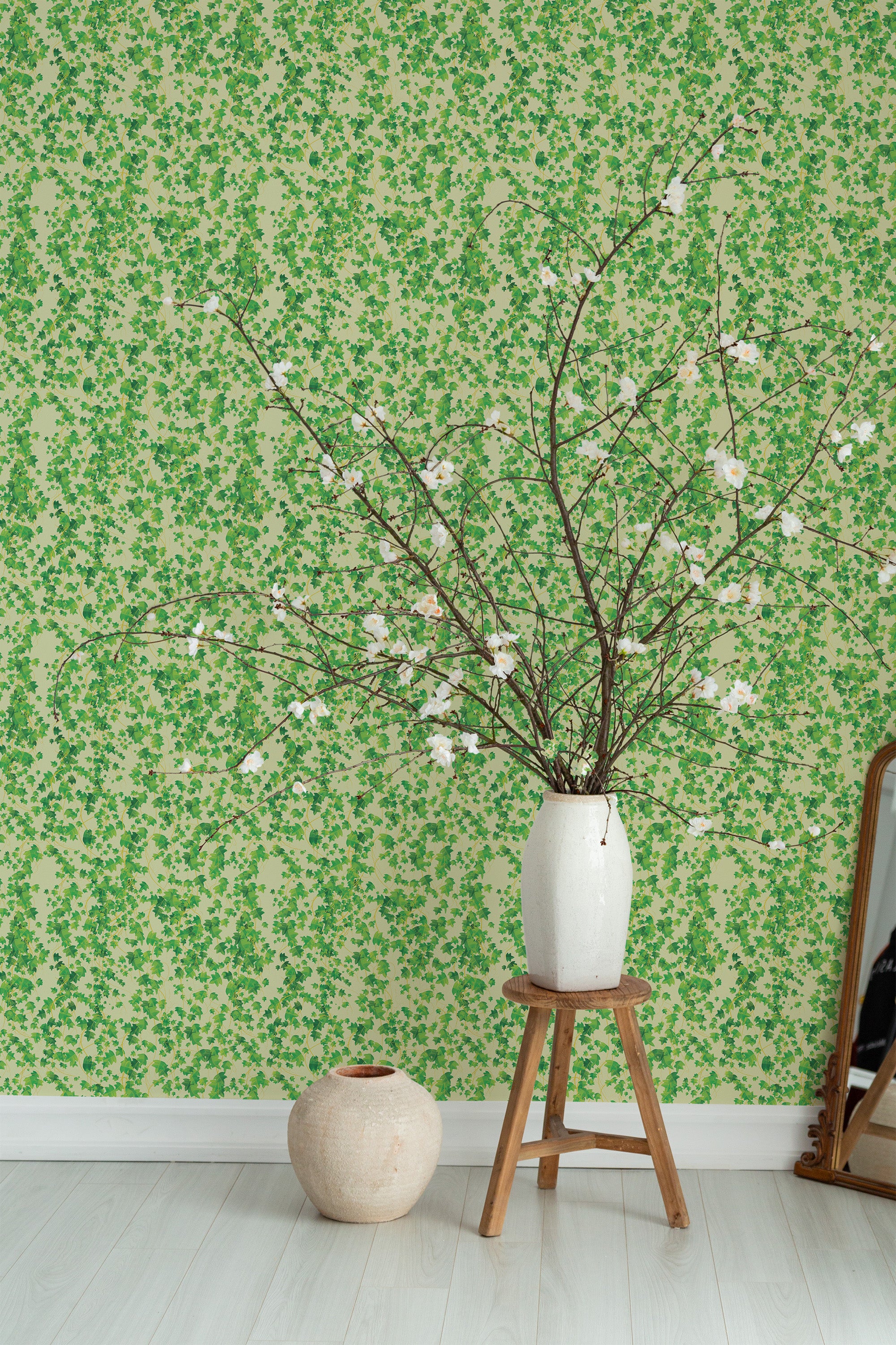 Self-adhesive wallpaper with a green and beige natural leaf pattern on a wall in a room, complemented by a vase with branches on a wooden stool.