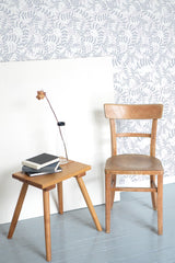 Self-adhesive wallpaper with a purple leaf pattern on a room wall, accompanied by a wooden chair and side table with books and a lamp.