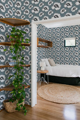 A room with walls covered in wallpaper adorned with white poppy flowers and delicate black stems and leaves against a muted blue-gray background. The traditional wallpaper complements the cozy, natural decor.