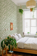 Green bamboo stalks and leaves arranged vertically on an off-white background, creating a calming, nature-inspired atmosphere in the cozy bedroom. Accentuating a minimalist, organic aesthetic, this traditional wallpaper harmoniously complements the room's wooden furniture and potted plants.