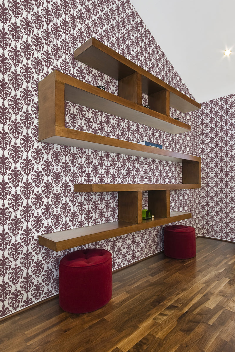 Wallpaper with intricate burgundy damask motifs set against a white background, creating a rich, ornate aesthetic. The wooden floating shelves and hardwood flooring complement the warm tones of the design, enhancing the vintage elegance of the room. Traditional wallpaper.