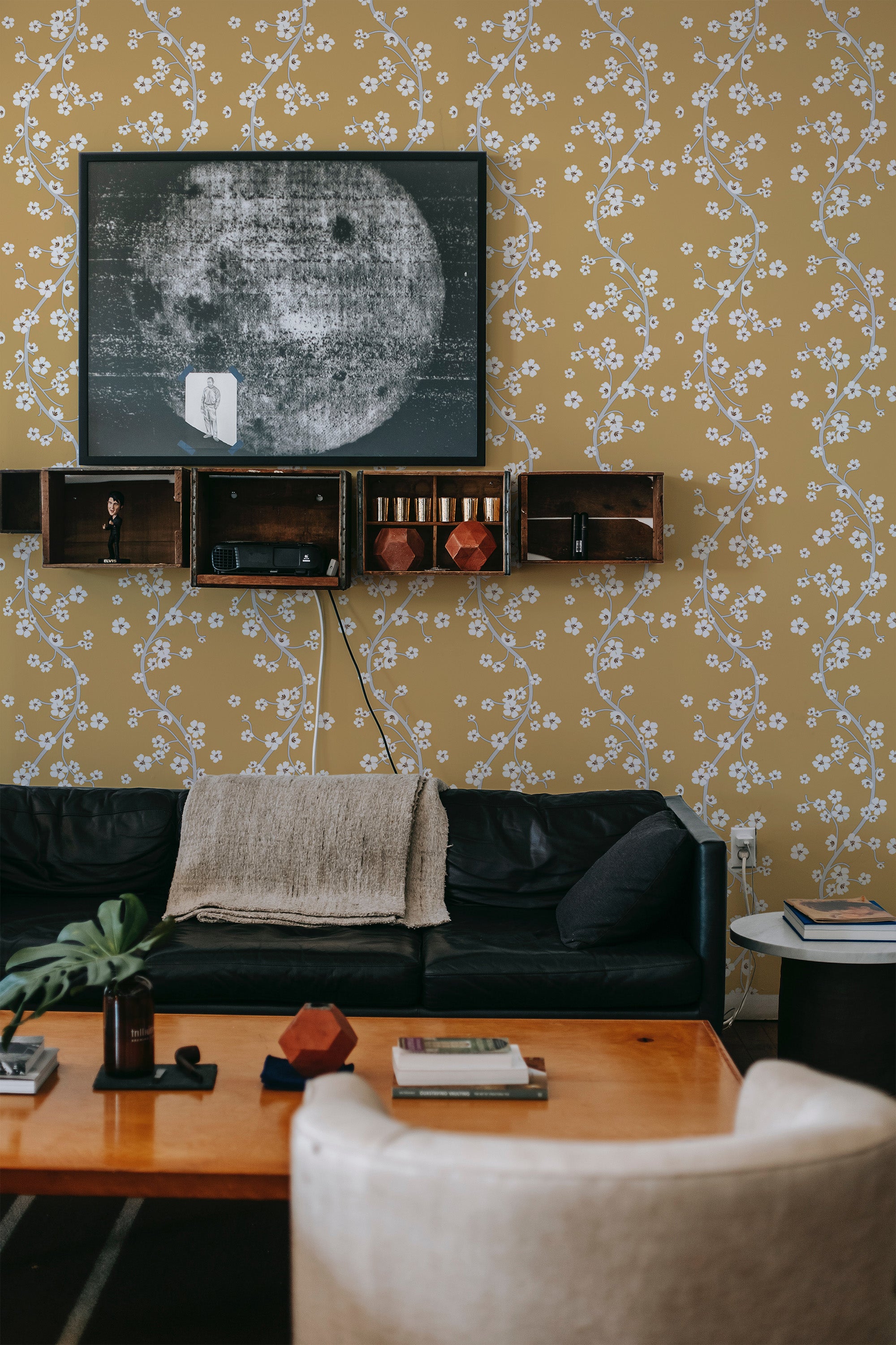 Yellow Chinoiserie wallpaper with a delicate pattern of winding white branches and small flowers covers the wall in a cozy living room. Traditional wallpaper.