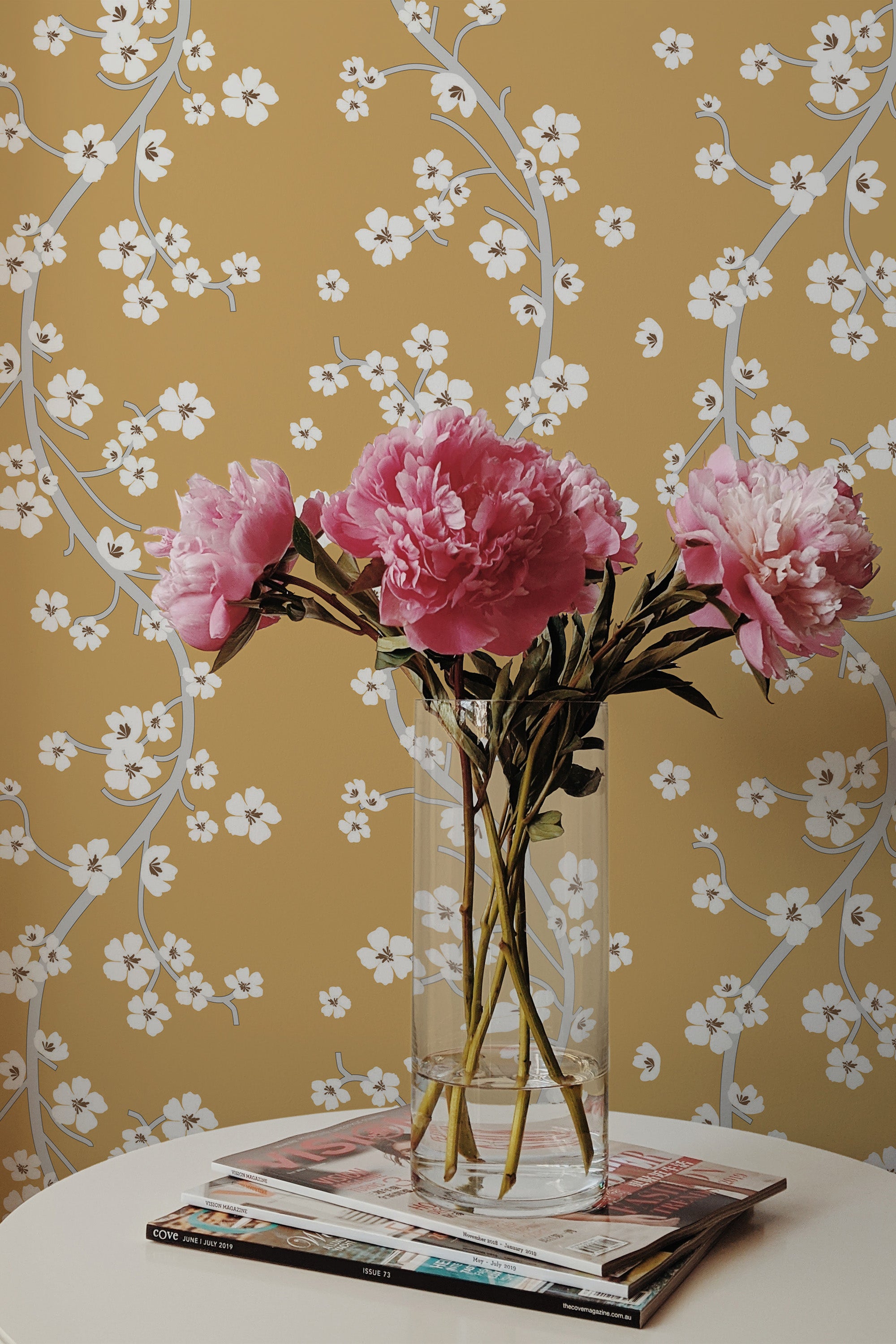 Self-adhesive Chinoiserie wallpaper with a mustard yellow background, white floral vines, and branches.