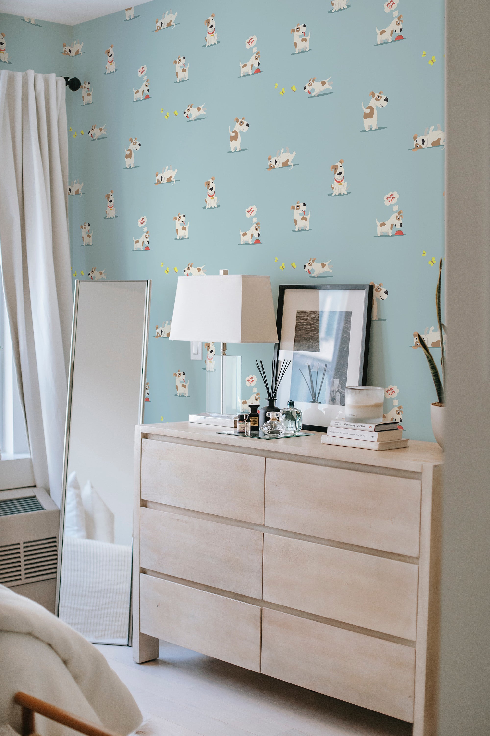 Light blue wallpaper with playful, cartoon-style puppies scattered across. The puppies are shown in various poses, surrounded by small yellow accents. The wallpaper complements the room's neutral decor, creating a whimsical contrast. Traditional wallpaper.