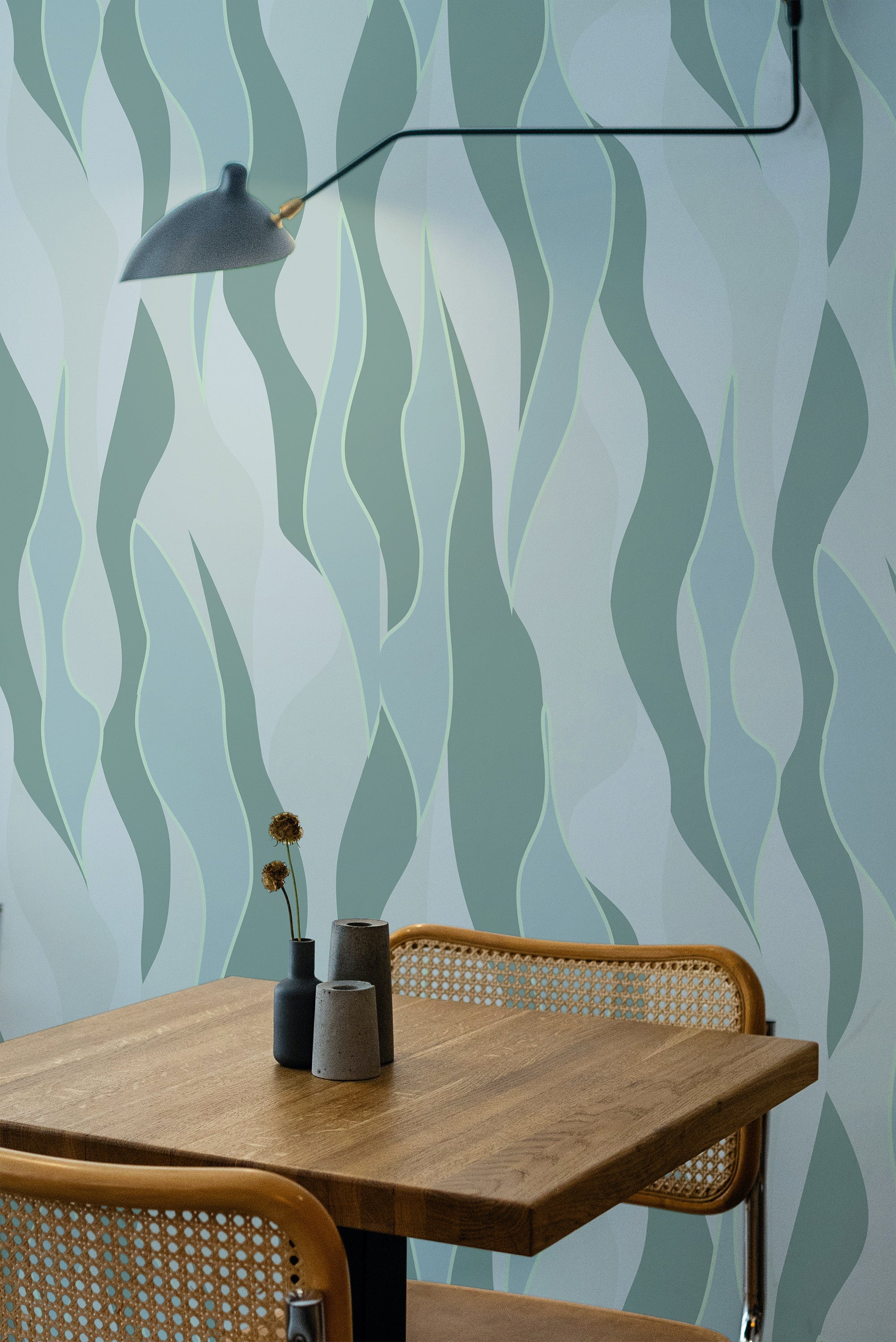 Self-adhesive wallpaper with a flowing, abstract design inspired by nature in shades of green and light blue, complementing a wooden dining table and wicker chairs.