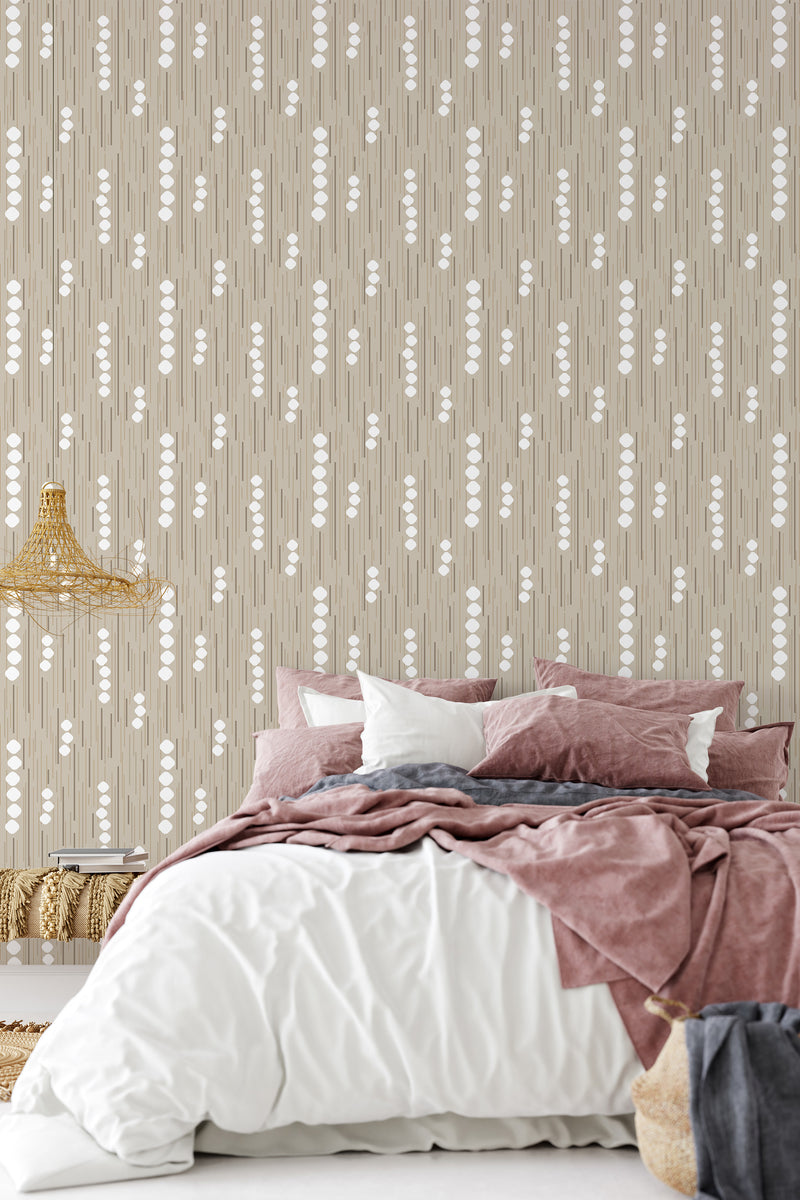 A room with neutral-colored wallpaper with vertical patterns of white dots alternated with thin lines on a beige background, creating a subtle yet elegant design. The room has a cozy atmosphere with a bed and pillows matching the wallpaper's color scheme. The wallpaper brings a classic touch to the room, enhancing the overall ambiance with traditional wallpaper.