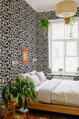 Black and white cow print wallpaper in a bedroom with a natural aesthetic, creating a bold, playful contrast against the light decor. Traditional wallpaper.