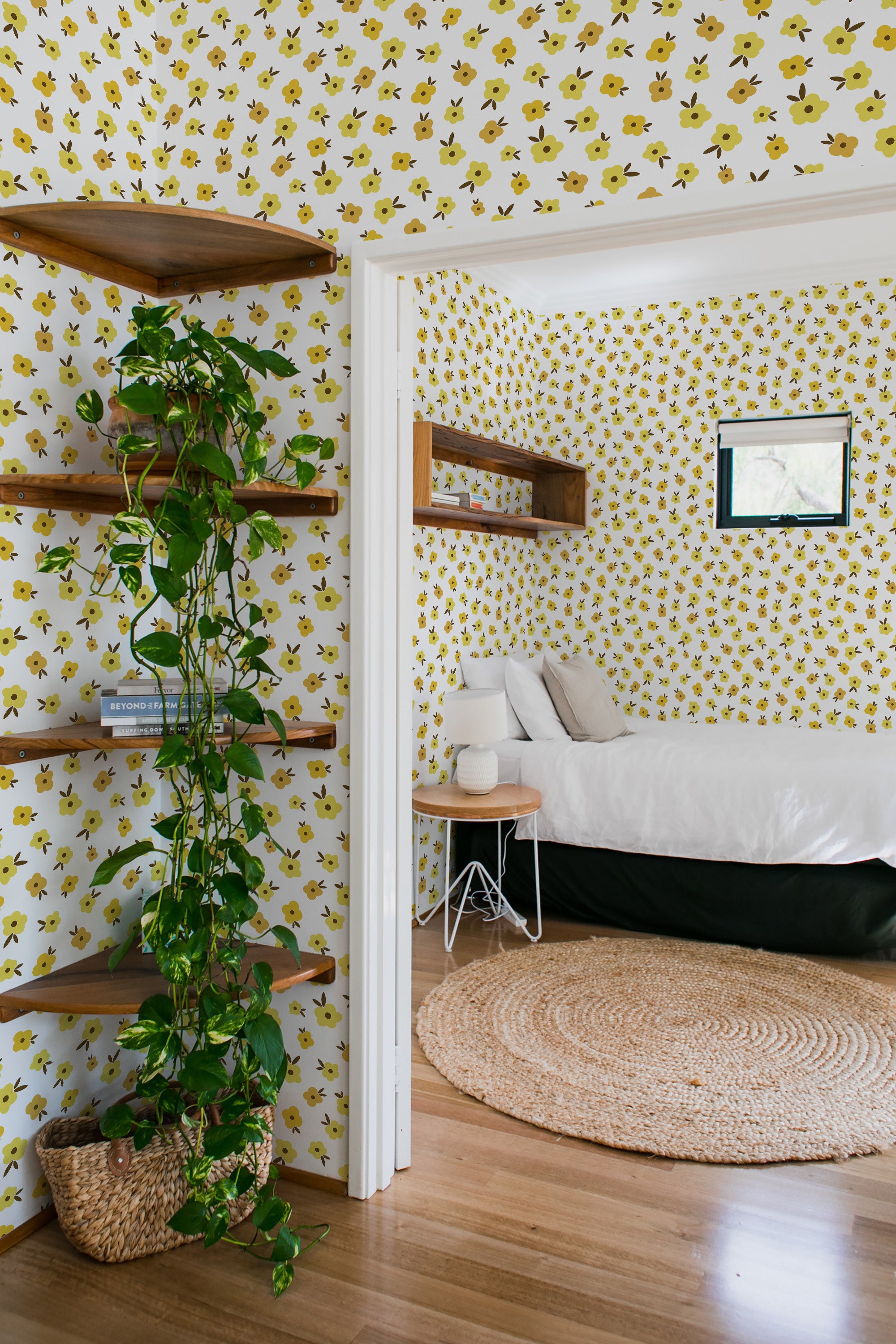 Room with white wallpaper adorned with small yellow flowers and green leaves, creating a bright and cheerful atmosphere. Shelves, a potted plant, and a bed are visible in the room. Traditional wallpaper.