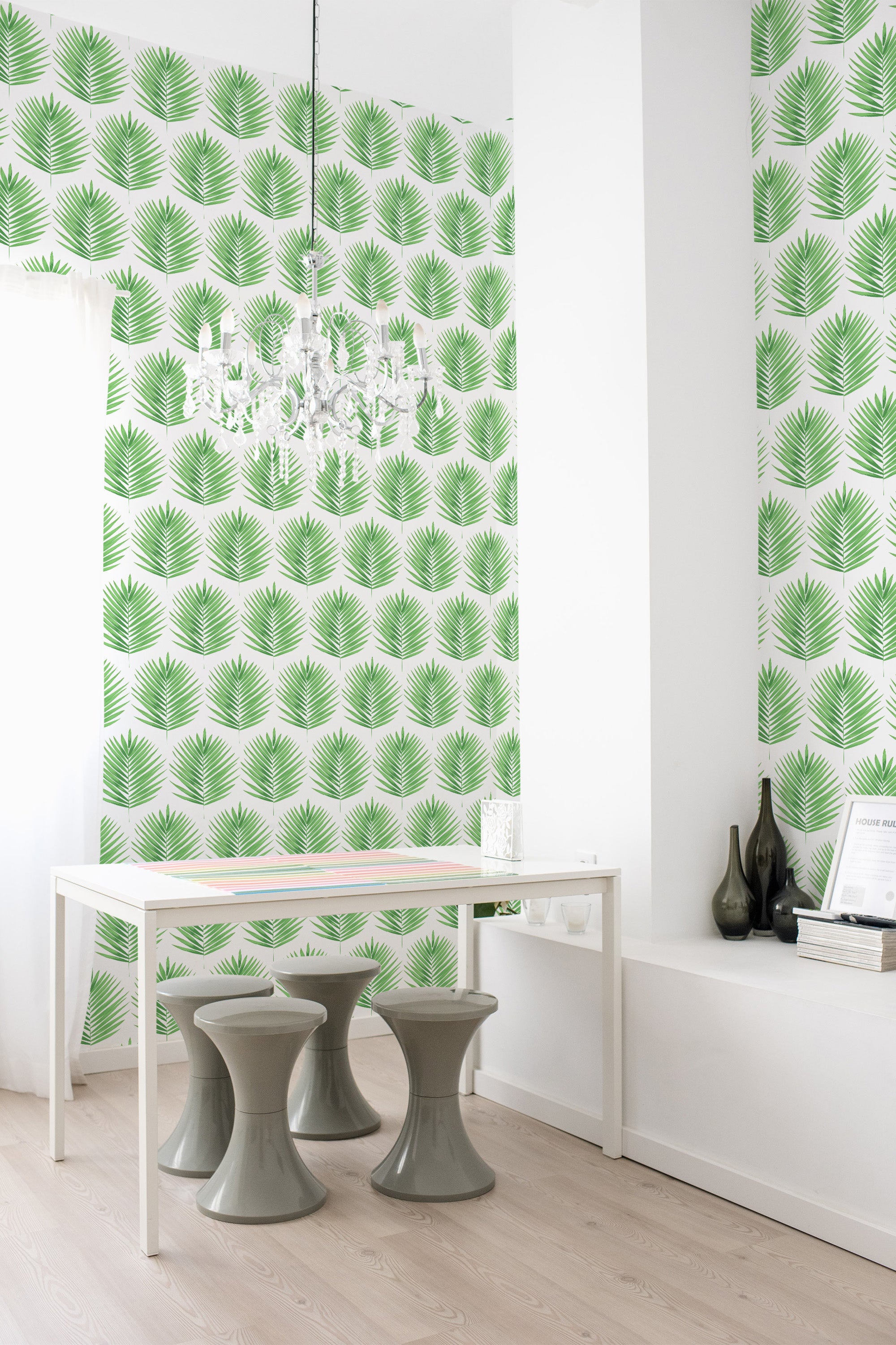 Green palm leaf pattern in a repeating design on white, covering the wall behind a minimalist white table and green stools, adding a fresh, tropical vibe to the room. Traditional wallpaper.