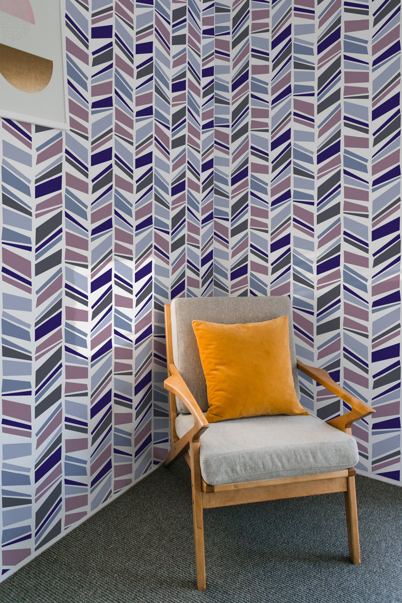 Room with Herringbone-patterned wallpaper in shades of purple, blue, and gray, covering the walls. A mid-century modern chair with a mustard-yellow pillow sits in the corner. Traditional wallpaper.