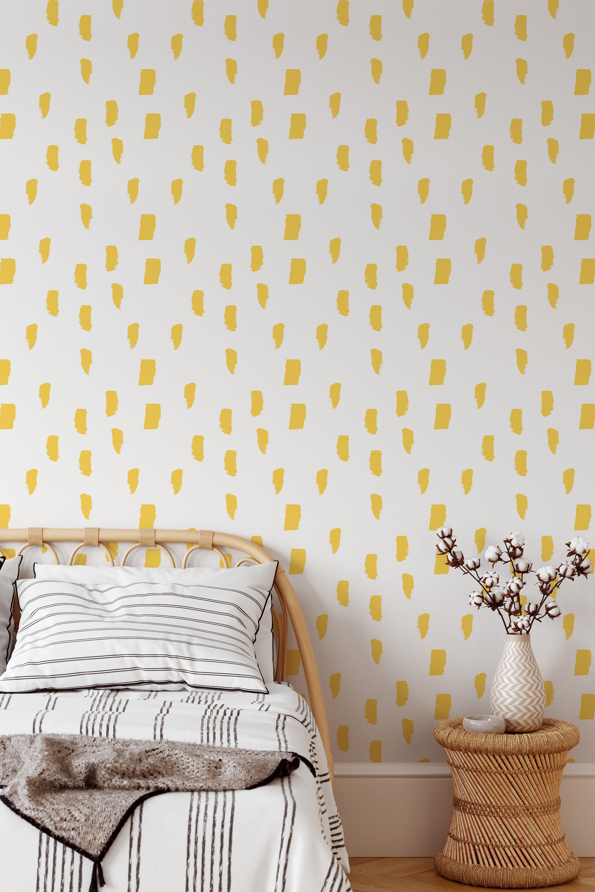 Self-adhesive wallpaper with a Painted dot design in yellow brushstrokes scattered across a white background, creating a playful and vibrant effect in the room. A cozy bed with a striped blanket and a small round wicker table holding a vase with branches enhance the space.