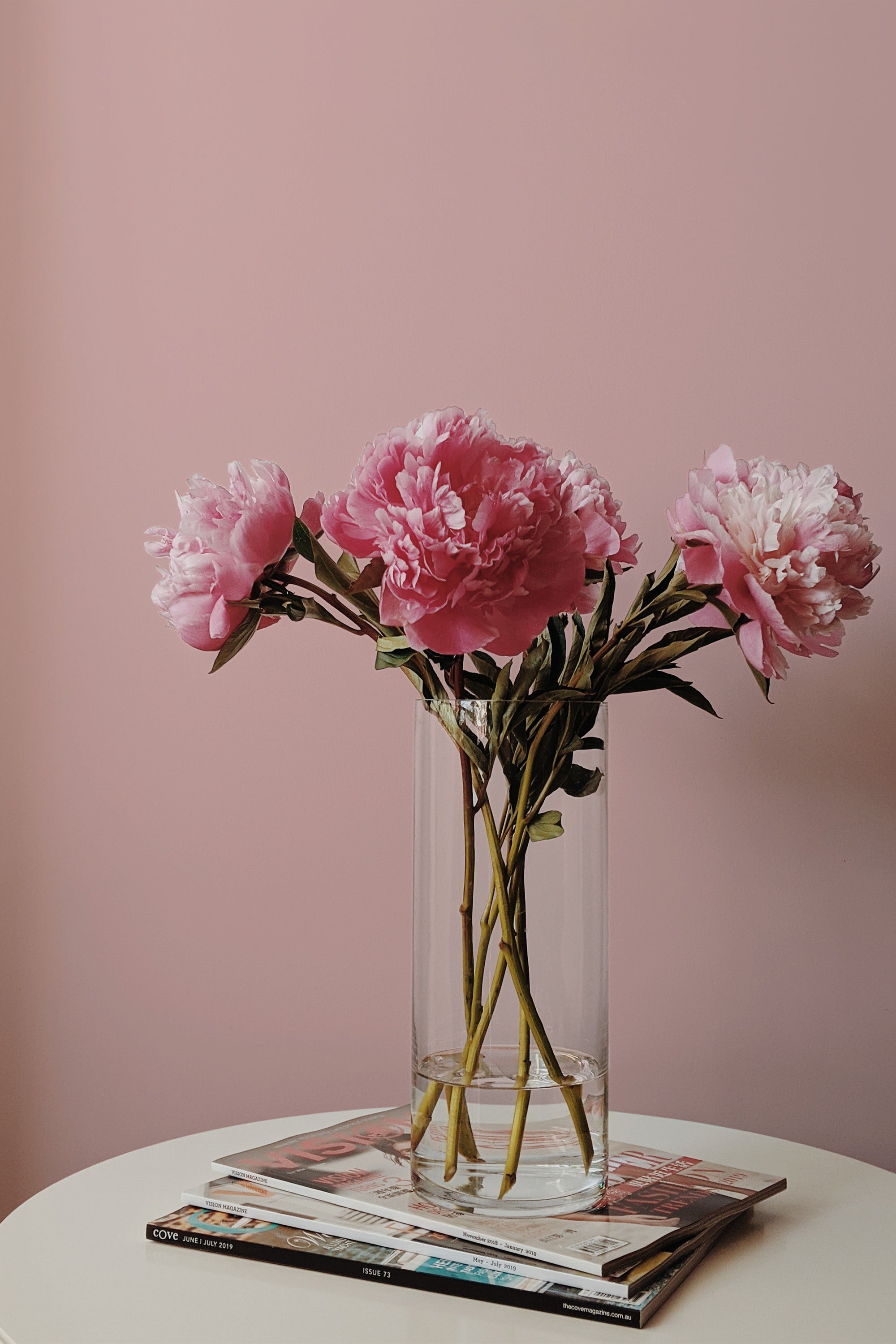 Self-adhesive, solid pink wallpaper creates a soft, soothing ambiance in the room. A vase with vibrant pink peonies on a white table adds a touch of natural elegance. The wallpaper serves as a subtle yet stylish backdrop, complementing the simple and refined decor.