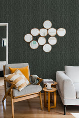 A room with a snake skin pattern wallpaper in a muted dark color creating a textured, sophisticated look, complemented by a grey armchair, yellow and plaid pillows, circular wall mirrors, and warm wood furniture. Traditional wallpaper.