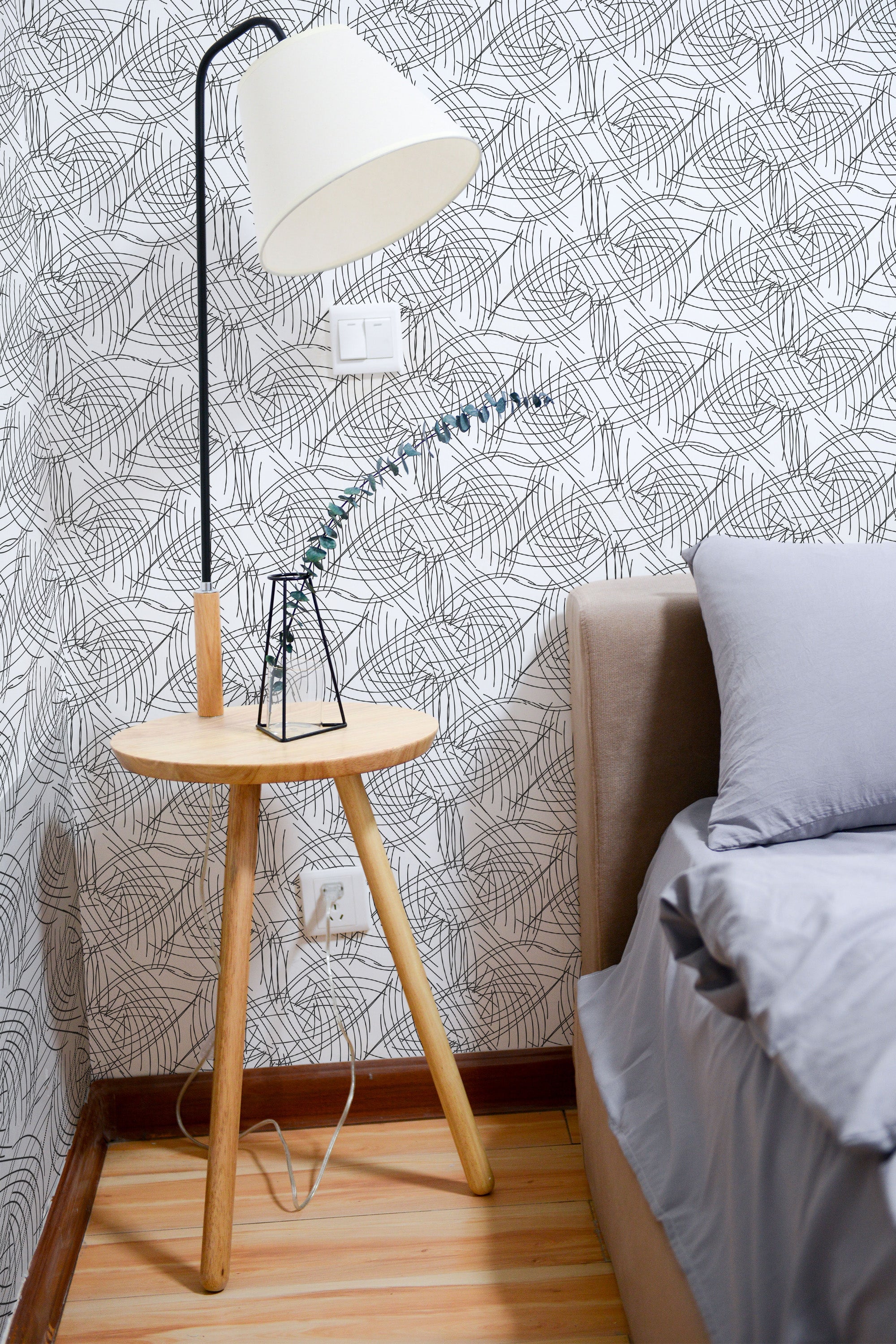 Self-adhesive wallpaper with a Line Art design of abstract, overlapping black curved lines on a white background, creating an intricate, modern pattern in a cozy bedroom setting.