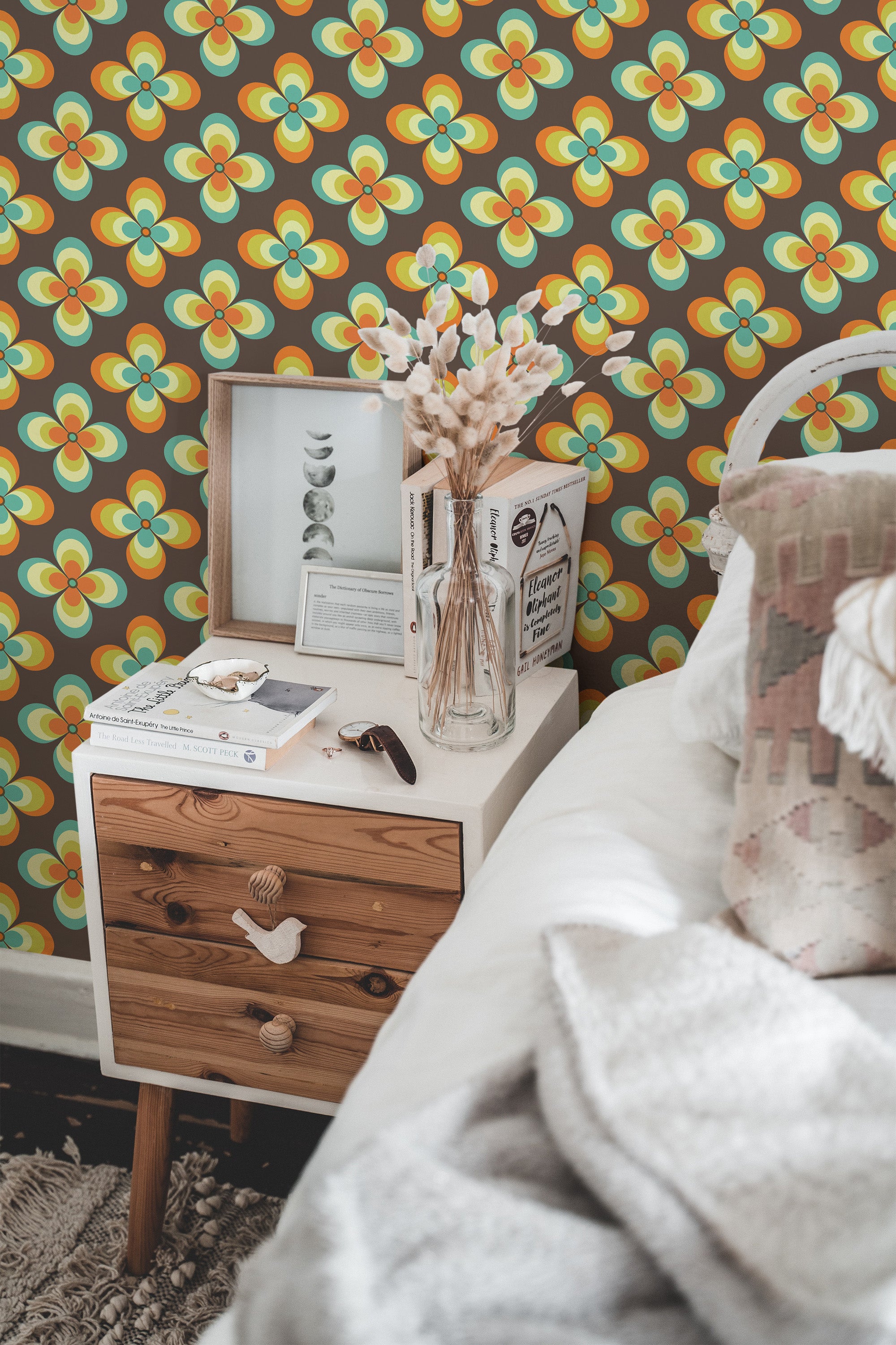 Self-adhesive wallpaper with a colorful retro flower design in orange, yellow, teal, and green hues forming symmetrical, overlapping floral patterns on a dark brown background.