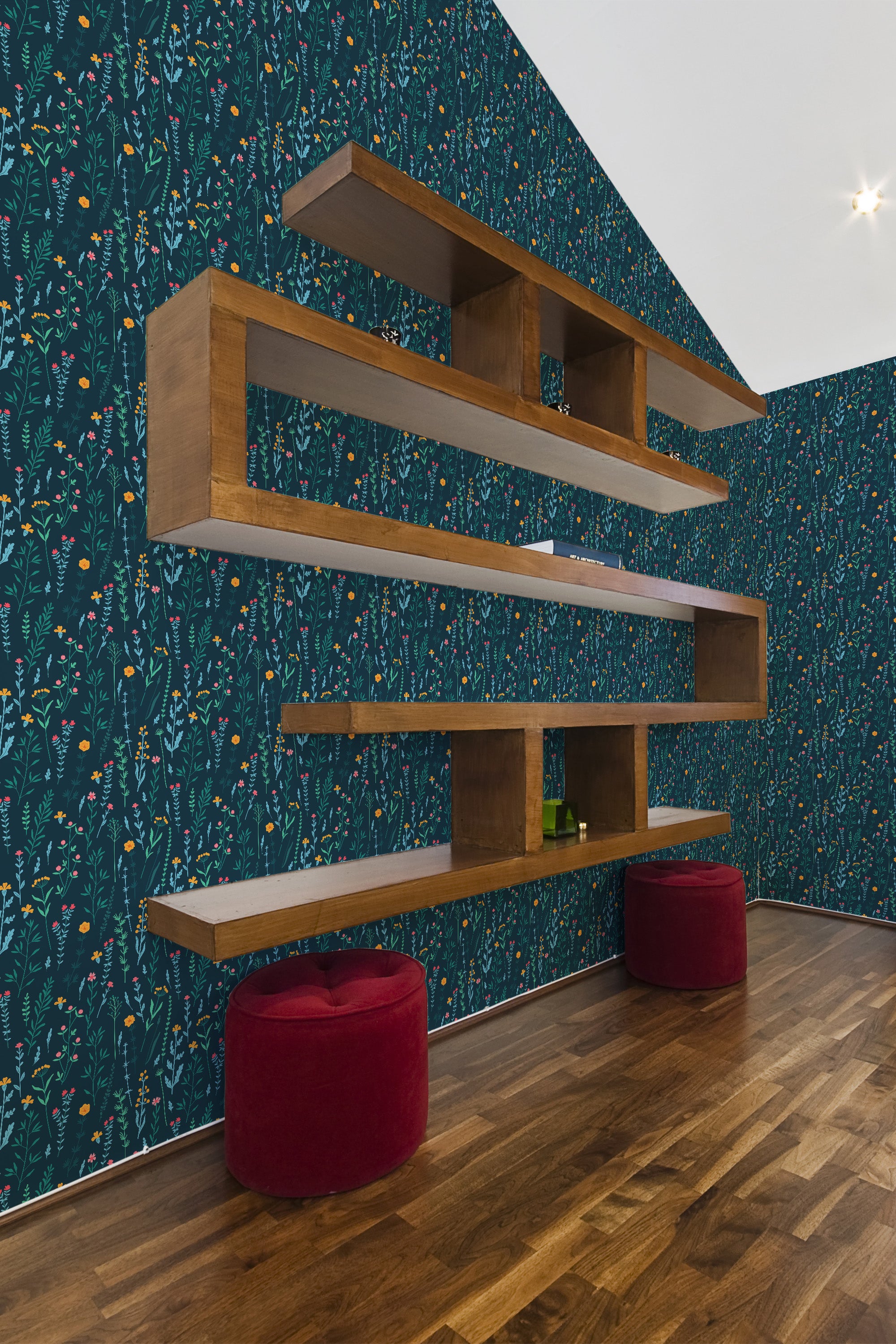 A room with dark blue wallpaper adorned with vibrant, intricate floral patterns, evoking a lush meadow. The design includes small flowers, leaves, and delicate stems spread uniformly across the wall, creating a warm and inviting ambiance. The wallpaper is complemented by wooden floating shelves and rich wood flooring, adding a cozy and rustic vibe to the space. Traditional wallpaper.