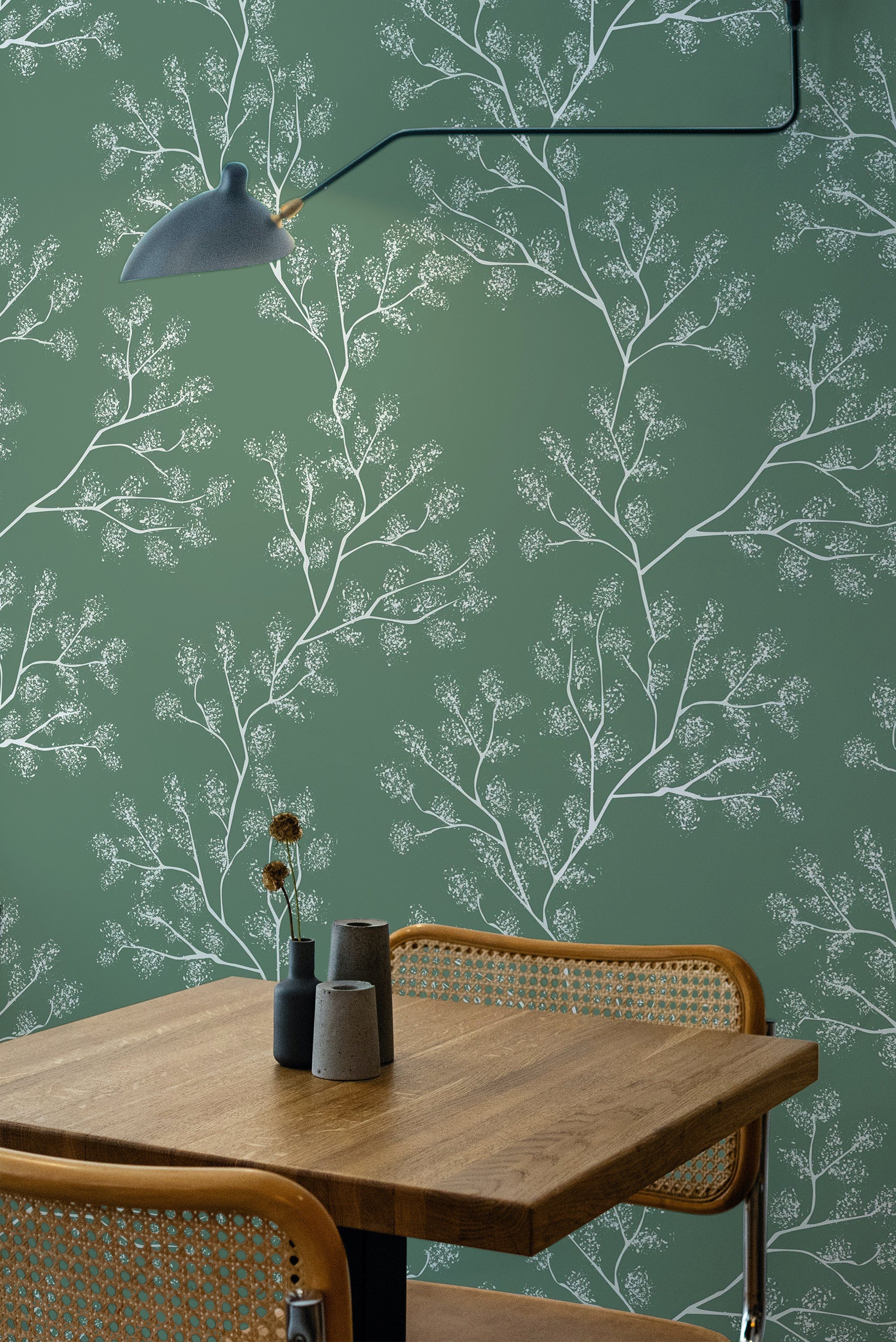 Self-adhesive wallpaper with a Green snow tree design, showing delicate white tree branches and intricate snowy details on a soft green background. The room includes a wooden table and chairs, adding a natural, serene ambiance.