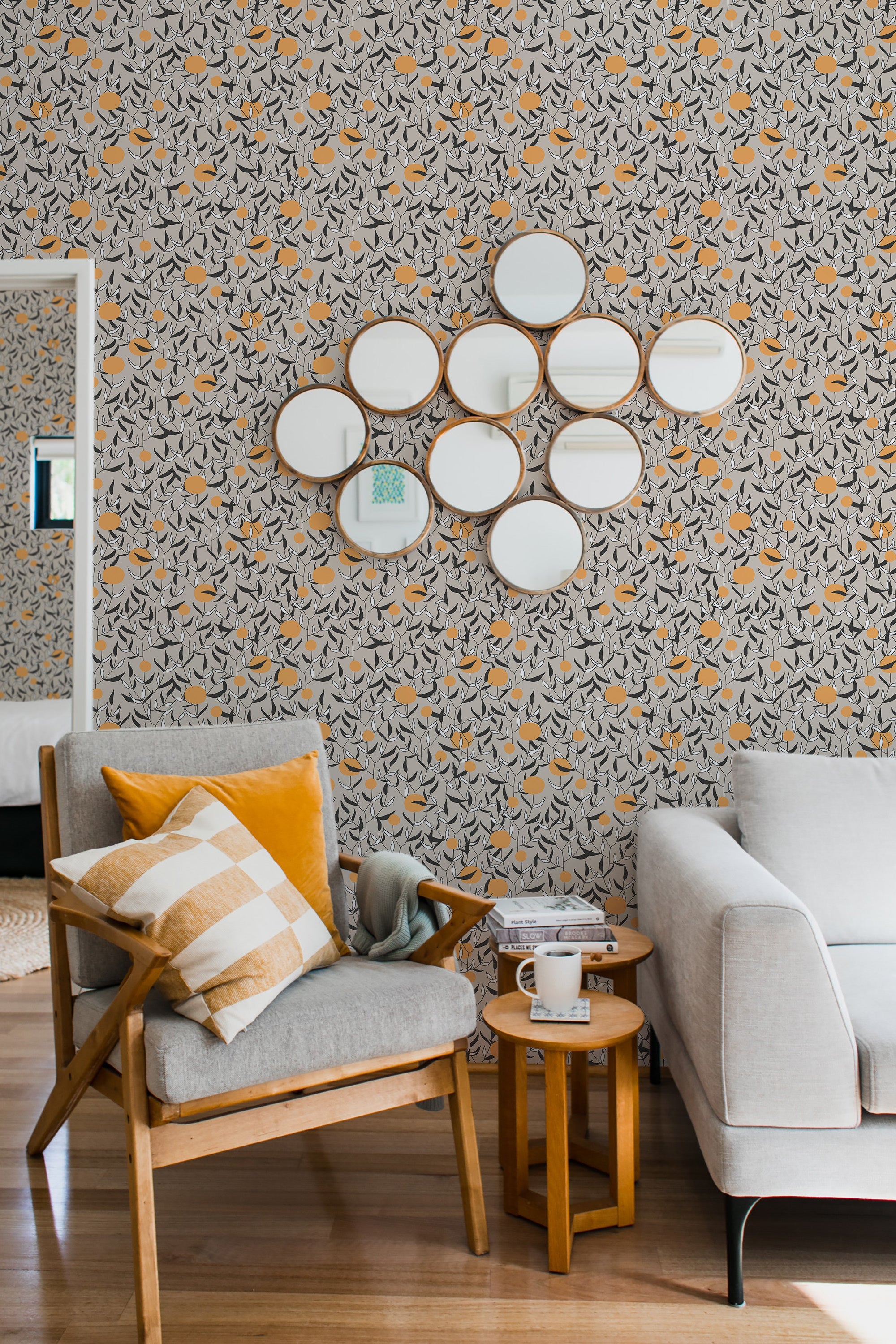 The wallpaper has a detailed design of orange tree branches with leaves and small oranges in neutral shades of gray and mustard. The pattern repeats across the entire wall, creating a visually pleasing and balanced look in the room. The design gives a cozy and inviting feel, complementing the modern yet warm interior decor. This is traditional wallpaper.