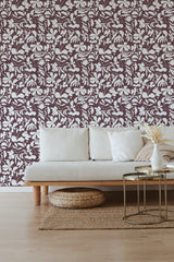 A room with a Burgundy nature shadows wallpaper, with a pattern of white leafy vines on a deep burgundy background, complementing a modern beige sofa and round coffee table on light hardwood floors. The wallpaper design adds an elegant and classic touch, integrating nature-inspired elements into the decor and creating a warm atmosphere with traditional wallpaper.