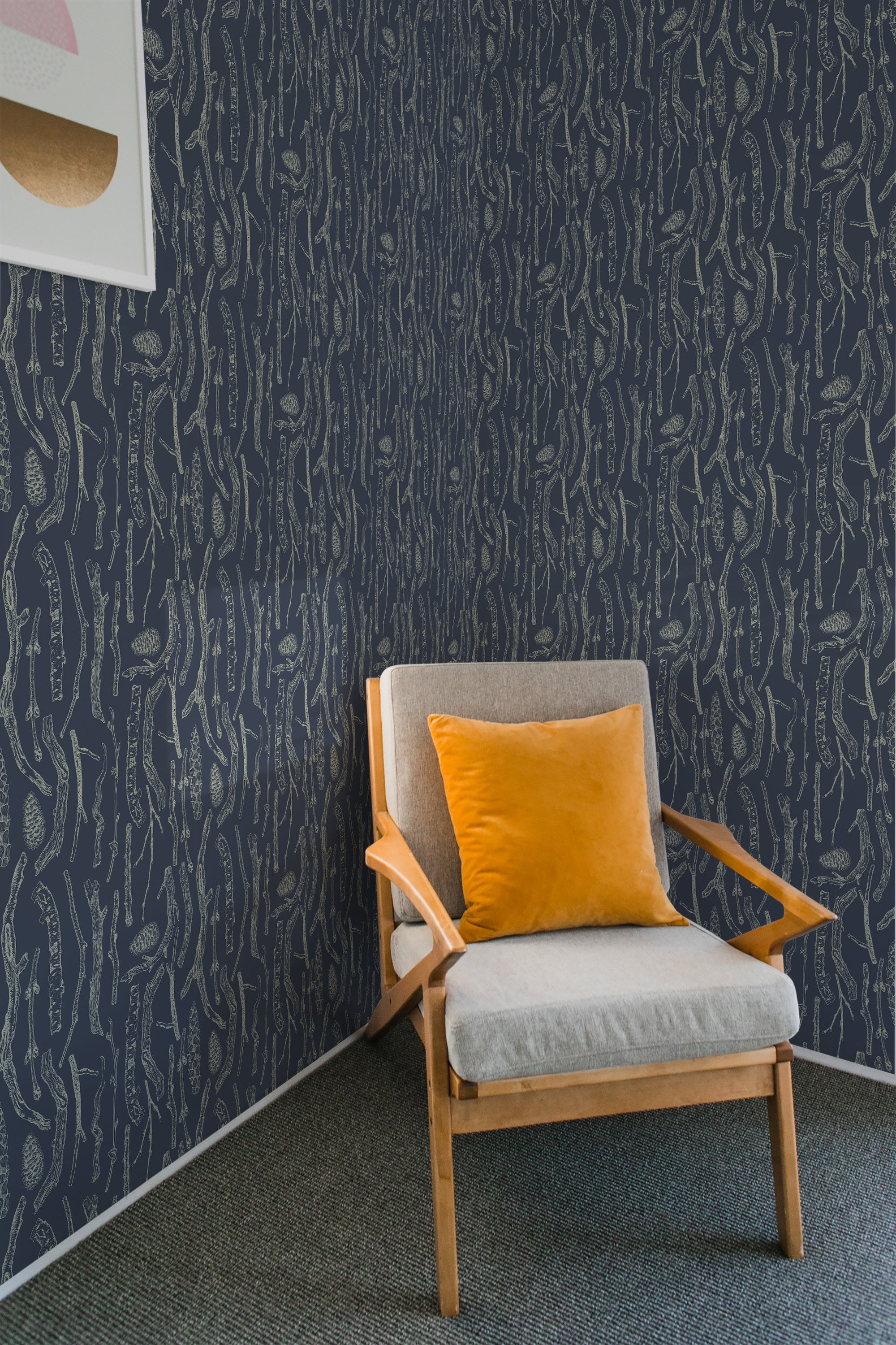 A room with wallpaper showing intricate, light-colored branches on a dark background, creating a nature-inspired pattern. The chair in the room has light grey cushions with a bright orange accent pillow, emphasizing the modern yet traditional wallpaper.