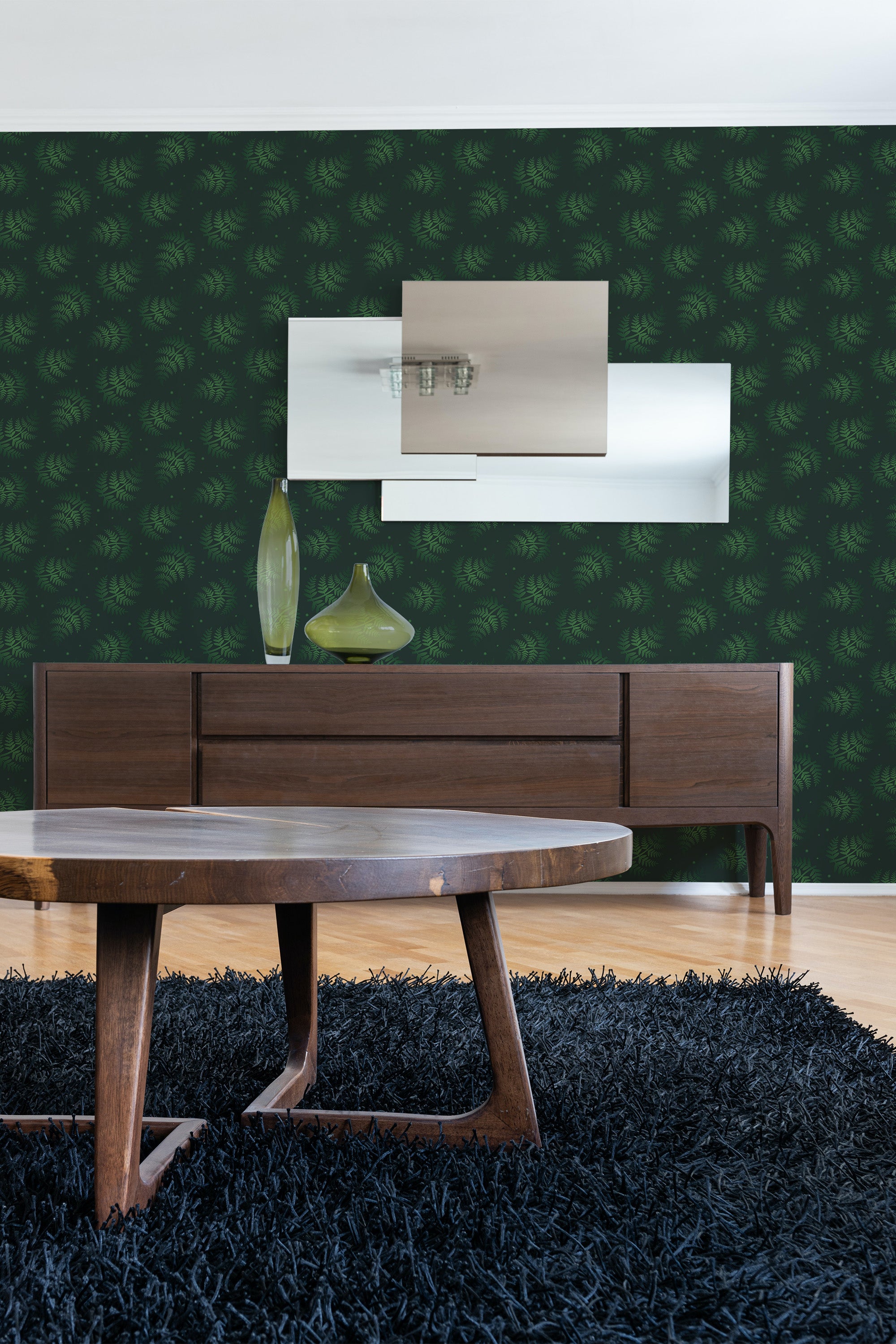 A room with dark green fern patterned wallpaper against a sleek, modern wooden console and a large mirror reflecting ambient light. The wallpaper adds a natural, lush touch to the space, offering a rich contrast to the wooden furniture and dark shag rug, creating a cozy yet elegant atmosphere. Traditional wallpaper.