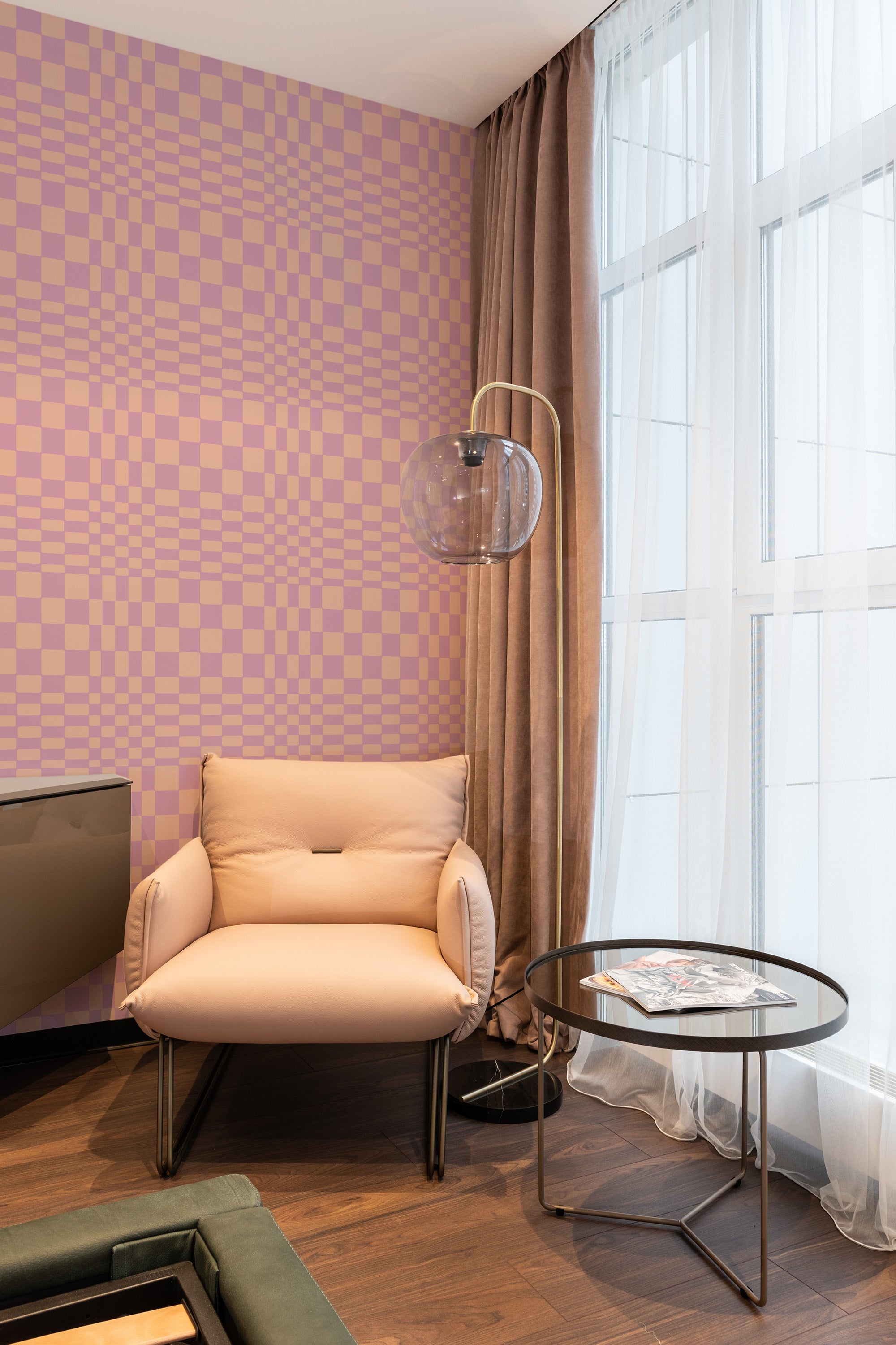 A room with wallpaper that creates a funky illusion design with alternating pink and beige checkered patterns, adding a playful and eye-catching element to the space. The wallpaper contrasts with the modern furnishings and window drapes, offering a modern twist on traditional wallpaper.