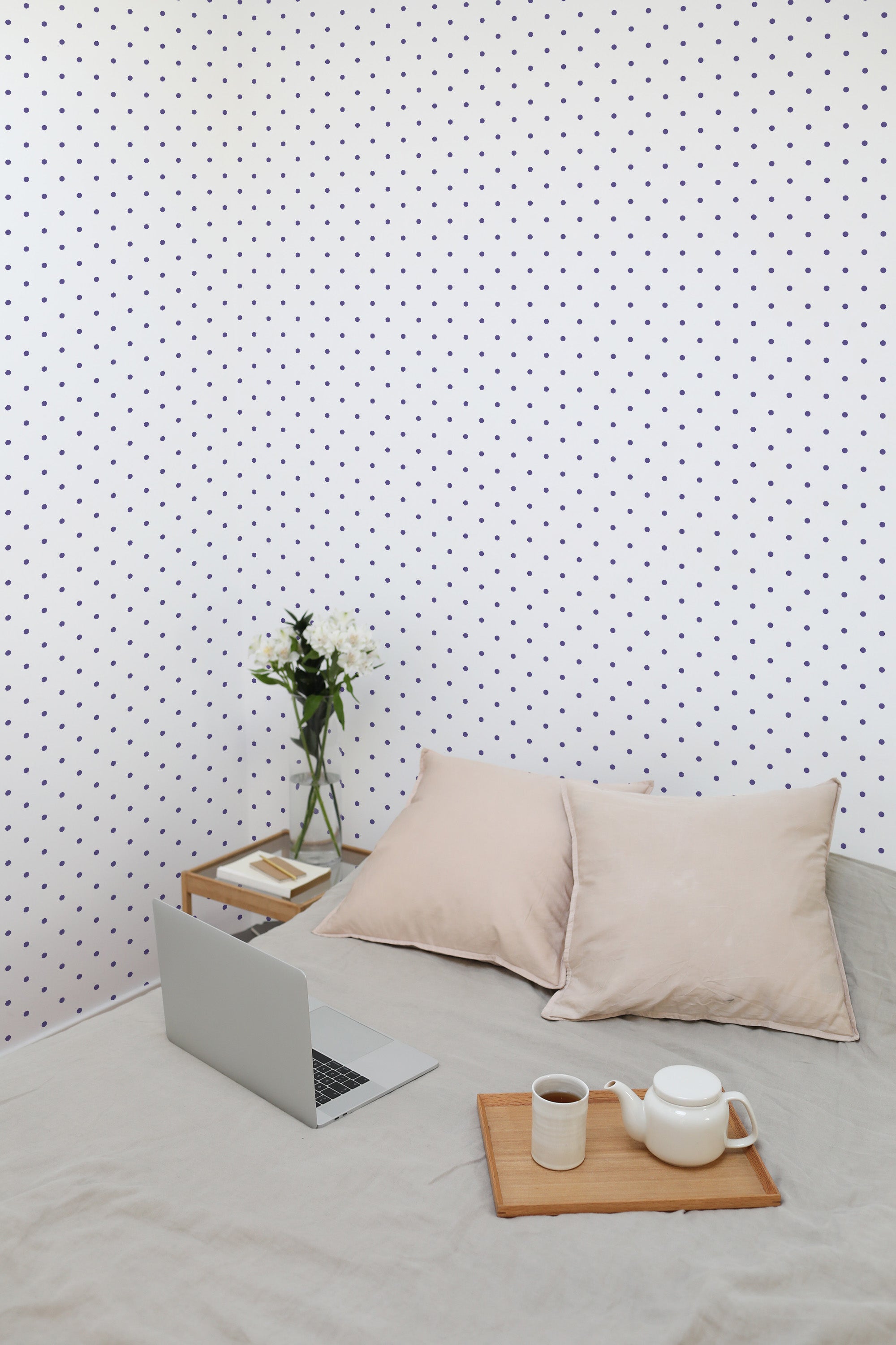 Self-adhesive wallpaper with a design of small purple polka dots evenly spaced on a light background, covering the wall in a room with neutral decor.
