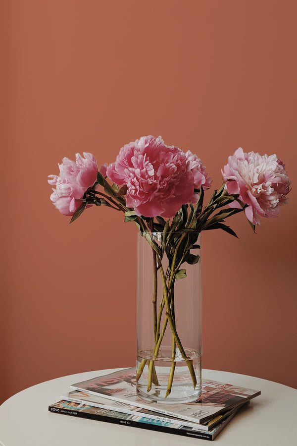 Self-adhesive Solid Terracotta wallpaper in a warm, earthy tone paired with a minimalist room setting including a glass vase with pink flowers on a small round table.