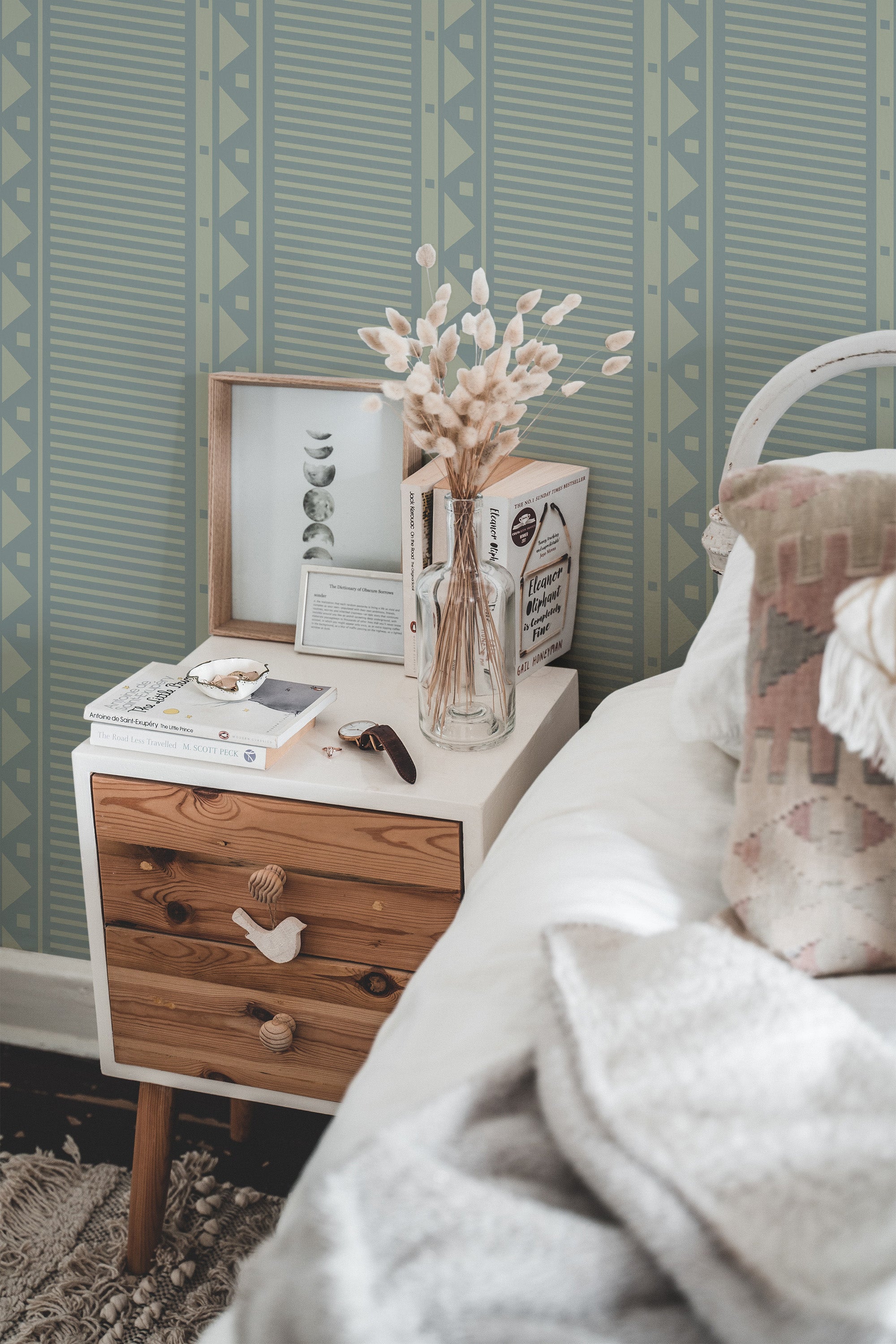 Self-adhesive wallpaper with geometric pattern in green tones on a bedroom wall, accompanied by a wooden bedside table and decor.