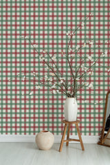 Self-adhesive Autumn plaid pattern wallpaper with green, red, and beige stripes, adorning a room's wall, complementing a vase with branches on a wooden stool.