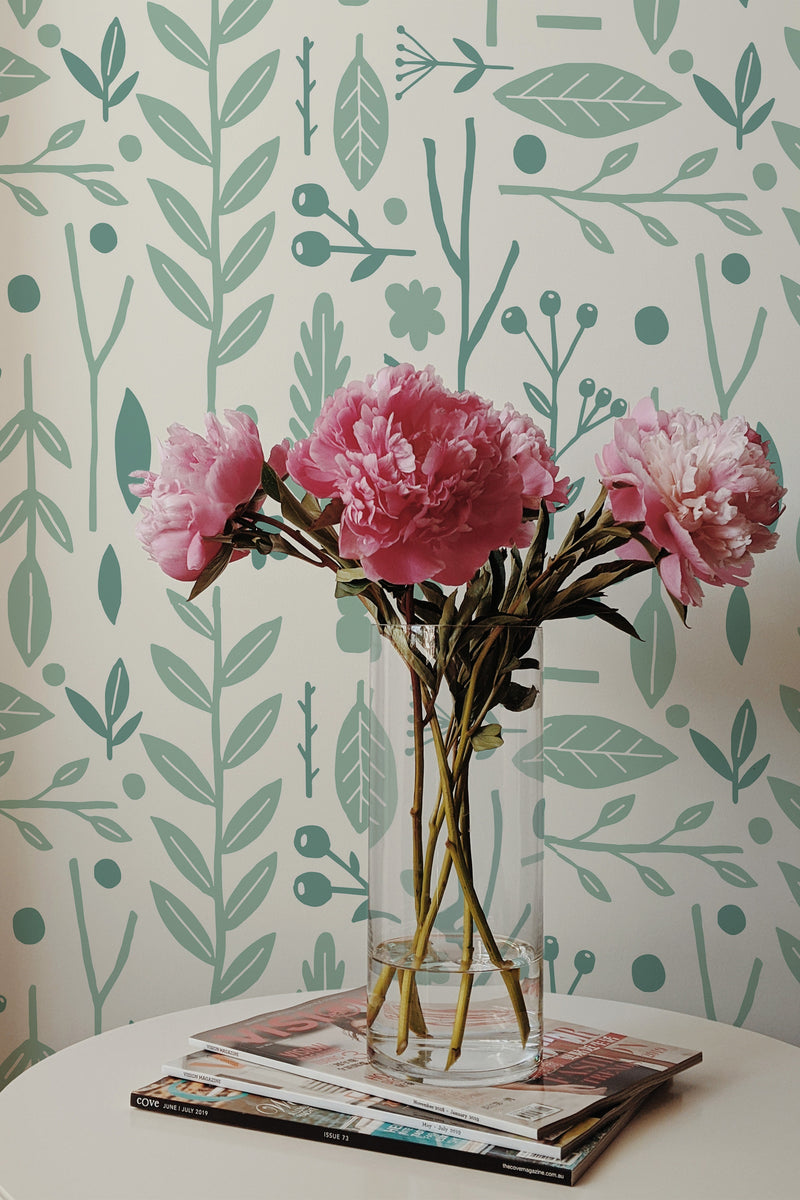 Self-adhesive wallpaper with a Scandinavian plant pattern including stylized green leaves and botanical motifs on a cream background, with a vase of pink peonies in the foreground.