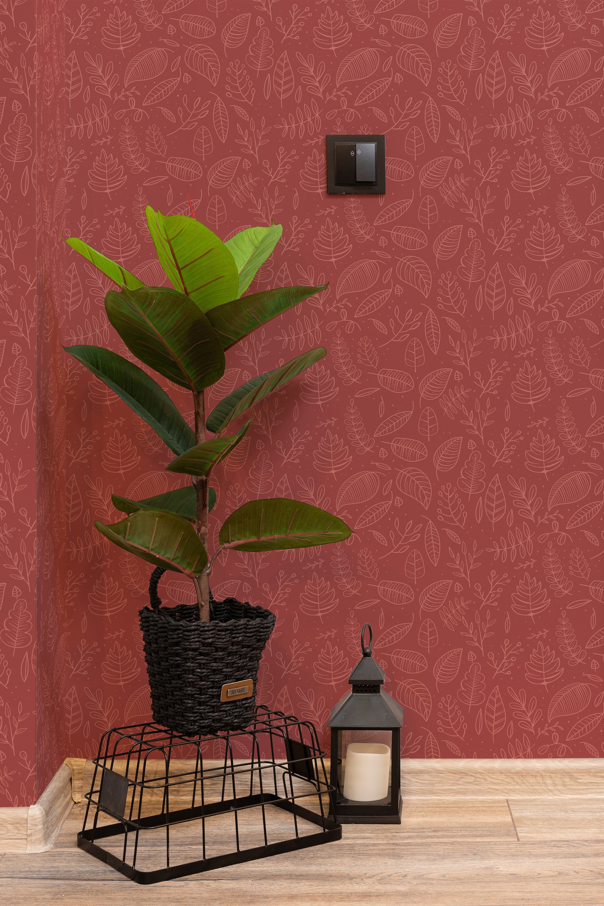 Self-adhesive wallpaper with a repeating pattern of stylized autumn leaves in line art on a warm red background, accented by a potted green plant and a black lantern.