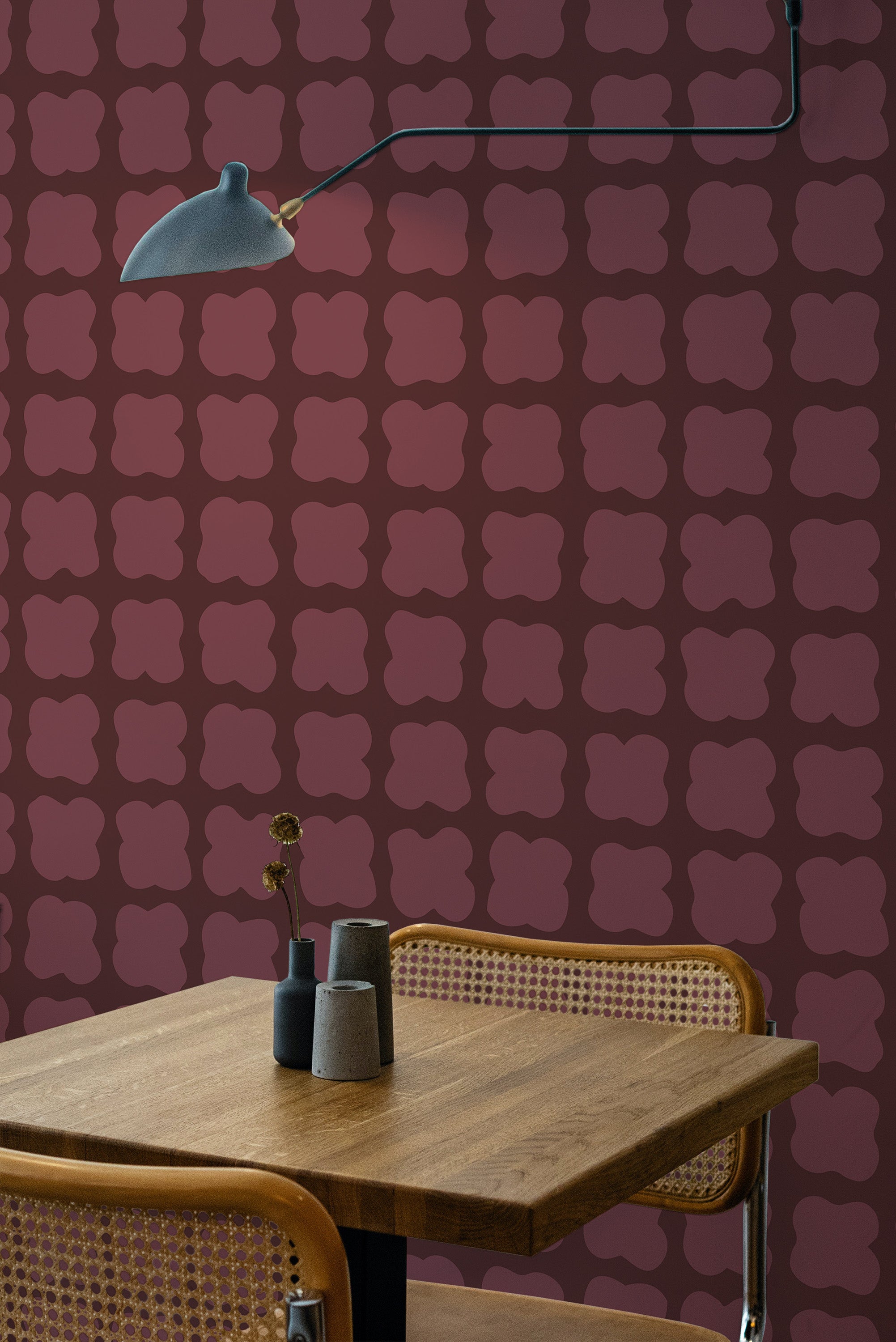 Self-adhesive wallpaper with maroon background and repeating geometric flower patterns in a room with a wooden table and a hanging lamp.