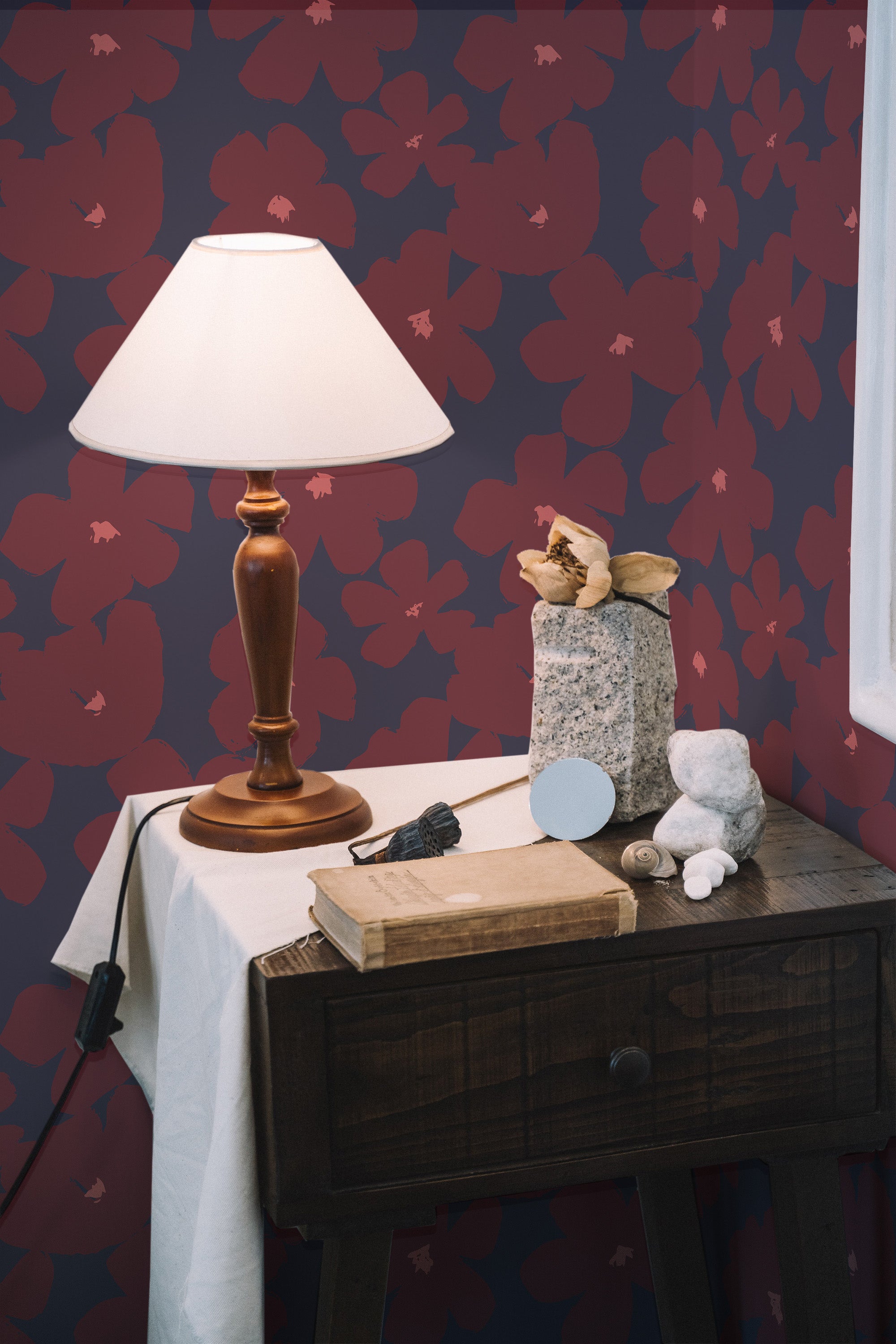 Self-adhesive wallpaper with a pattern of large red and pink brushstroke flowers on a dark blue background, in a room with a wooden desk and lamp.