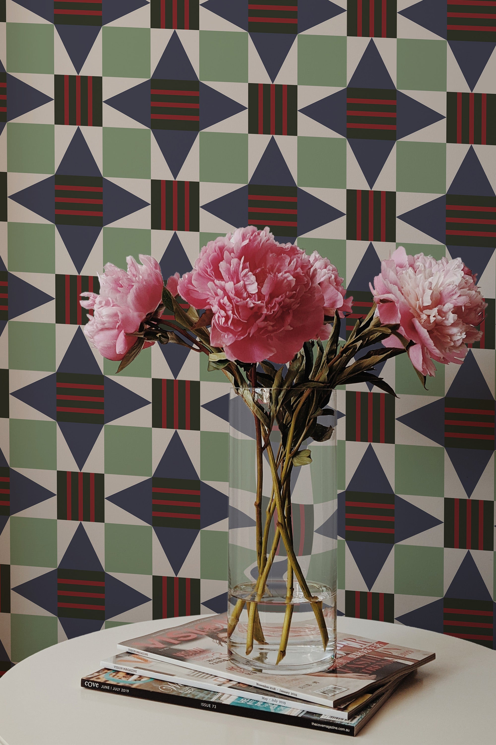 Self-adhesive wallpaper with a geometrical star tile pattern in shades of green, beige, and red with a bouquet of pink peonies in the foreground.