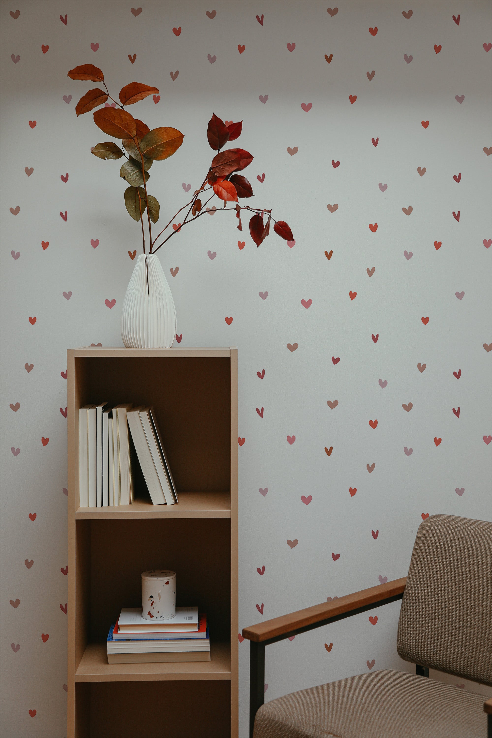 Self-adhesive wallpaper with a repeating tiny heart pattern on a neutral background in a room with a bookshelf and a vase of leaves.