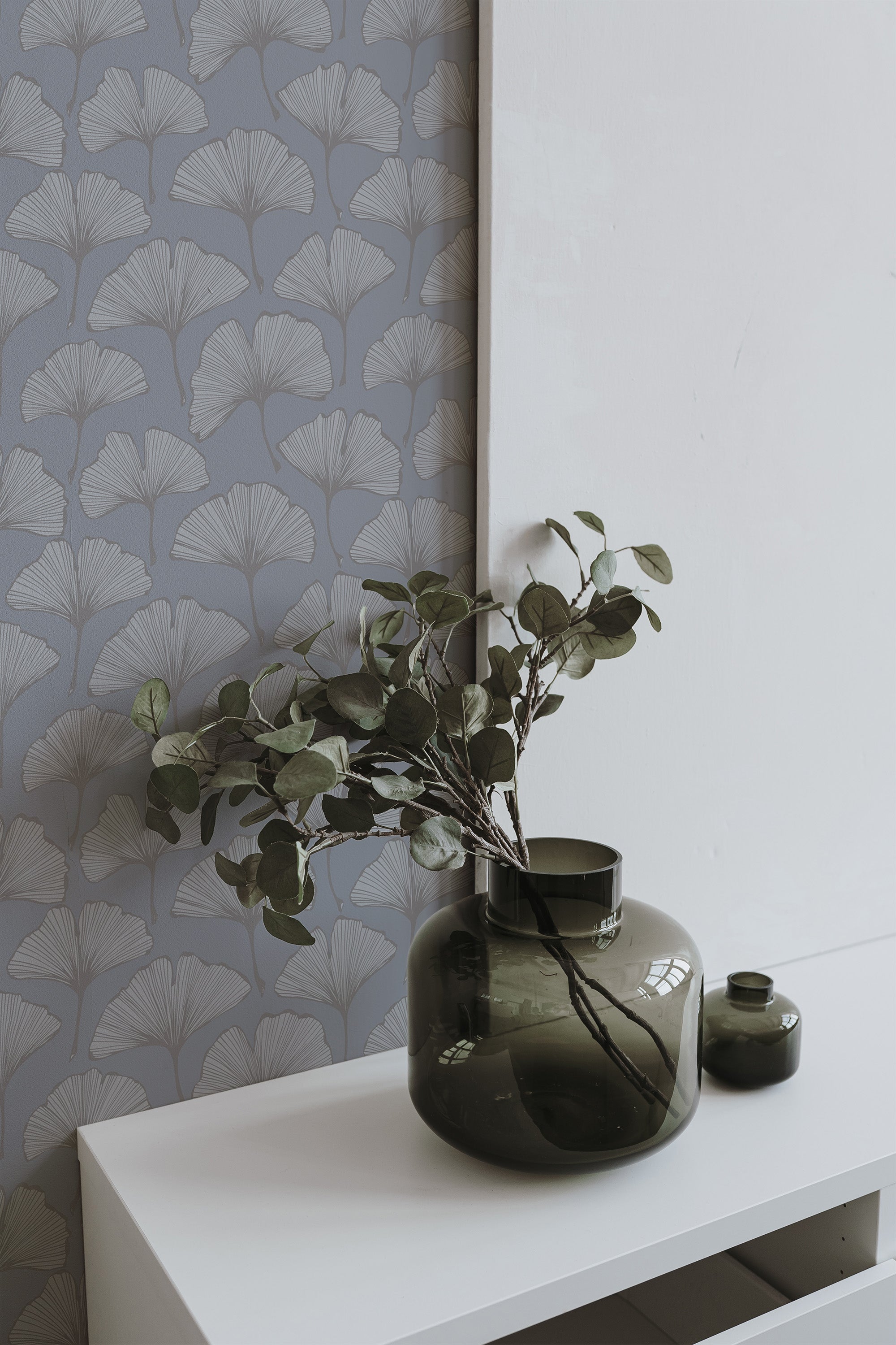 Self-adhesive wallpaper with a ginkgo leaf pattern in shades of gray, creating a minimalist and modern look on a wall, with a green vase and plant on a white shelf.
