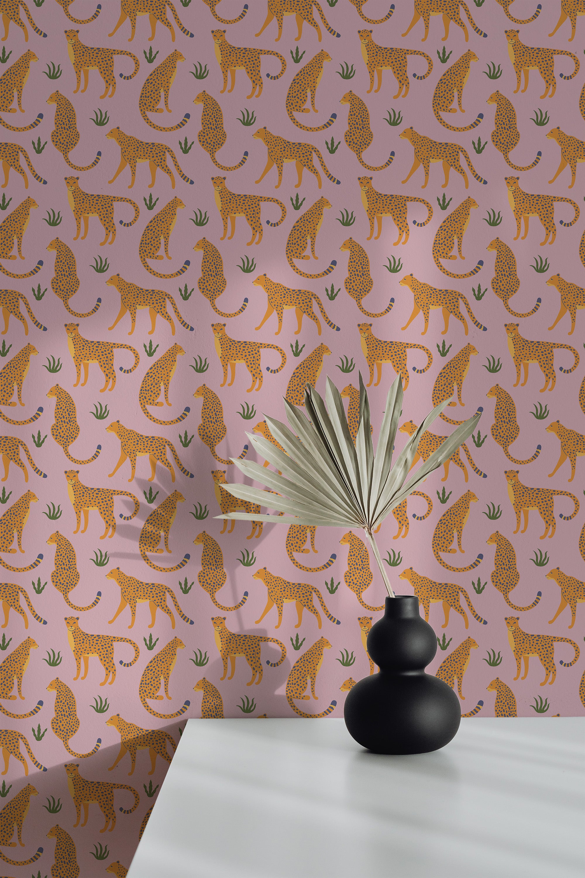 Self-adhesive Bold Cheetah wallpaper with orange cheetah motifs on a pink background, accented by a decorative fan and black vases on a white surface.