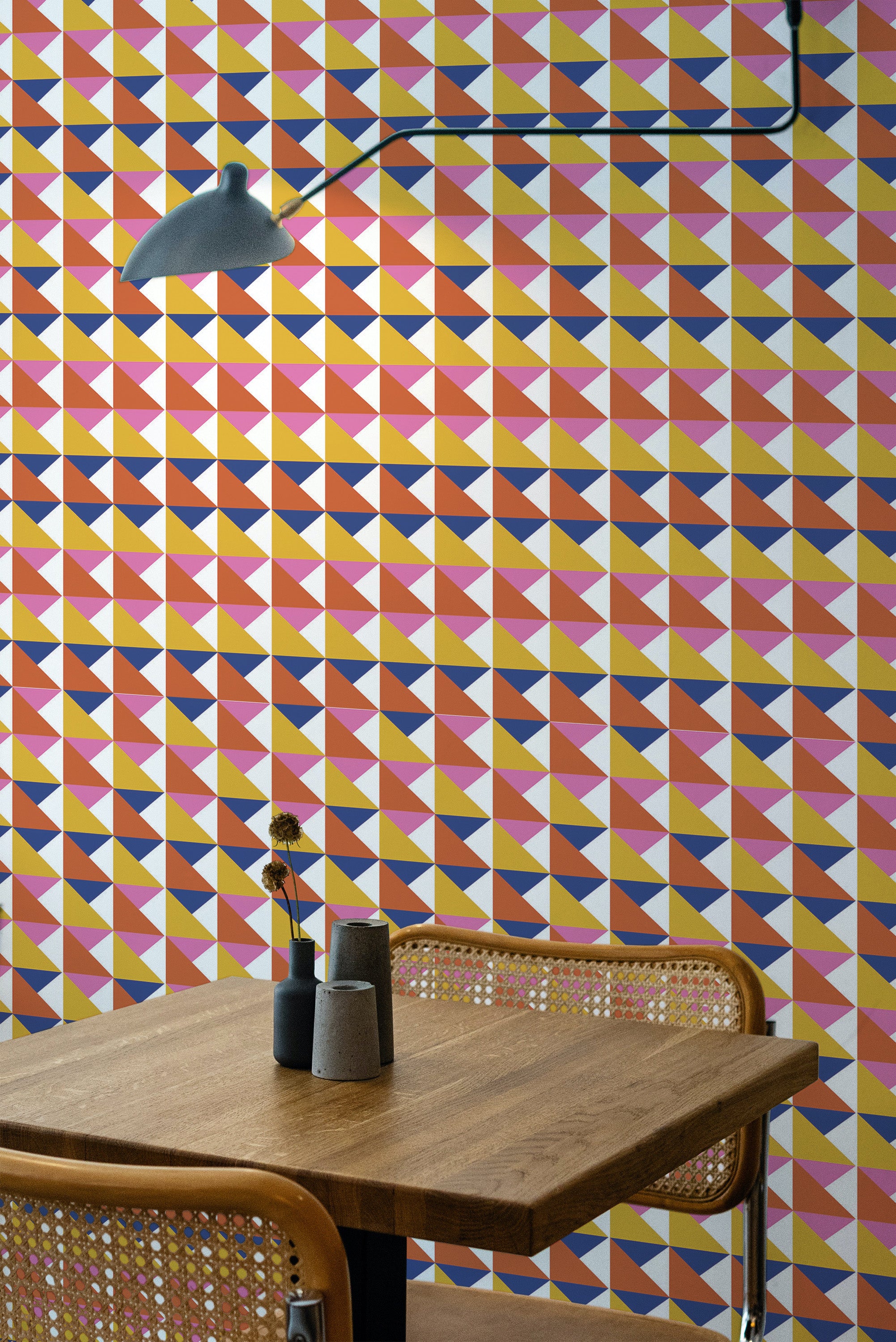 Self-adhesive wallpaper with a pattern of multicolored retro triangles on a room wall, accompanied by a wooden table and a pendant lamp.