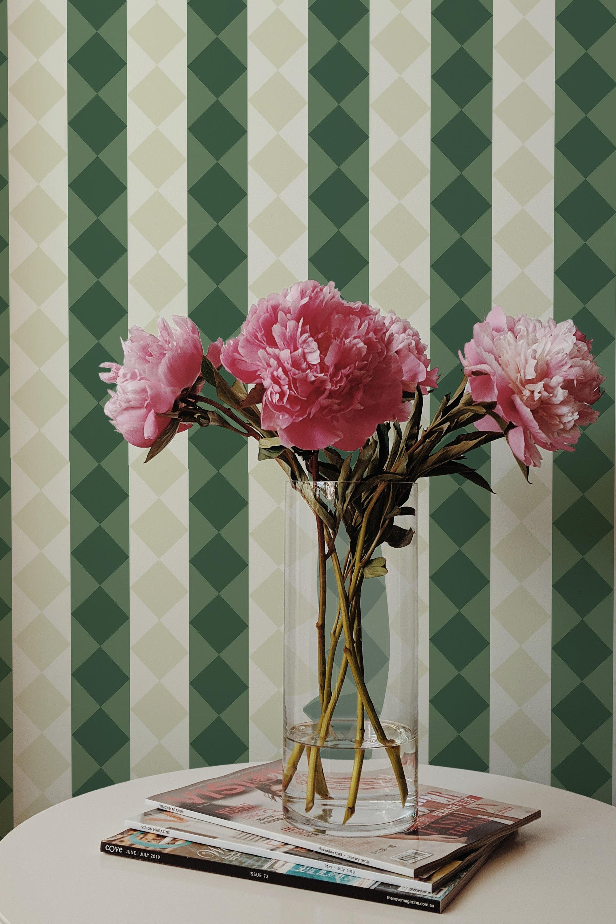 Self-adhesive retro geometric wallpaper with alternating green and beige vertical stripes in a room, complemented by a vase of pink peonies on a table.