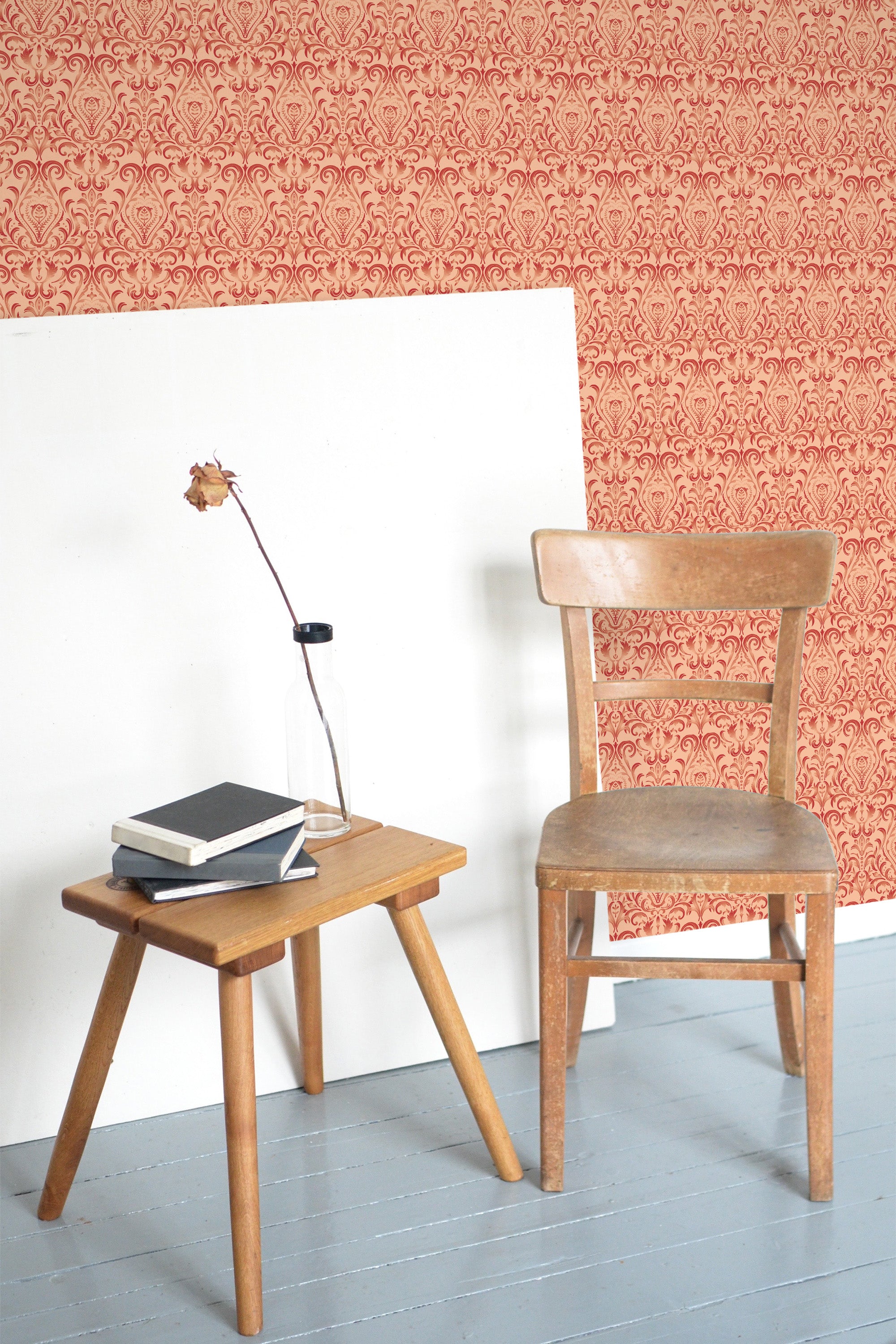 Self-adhesive Peachy Damask wallpaper with intricate patterns on a room's wall, accompanied by a wooden chair and table with books and a lamp.