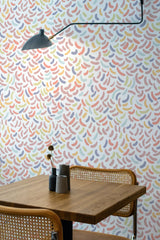 Self-adhesive Jellybean wallpaper with multicolored curved shapes on a room wall, above a wooden table and chair set with a vase.