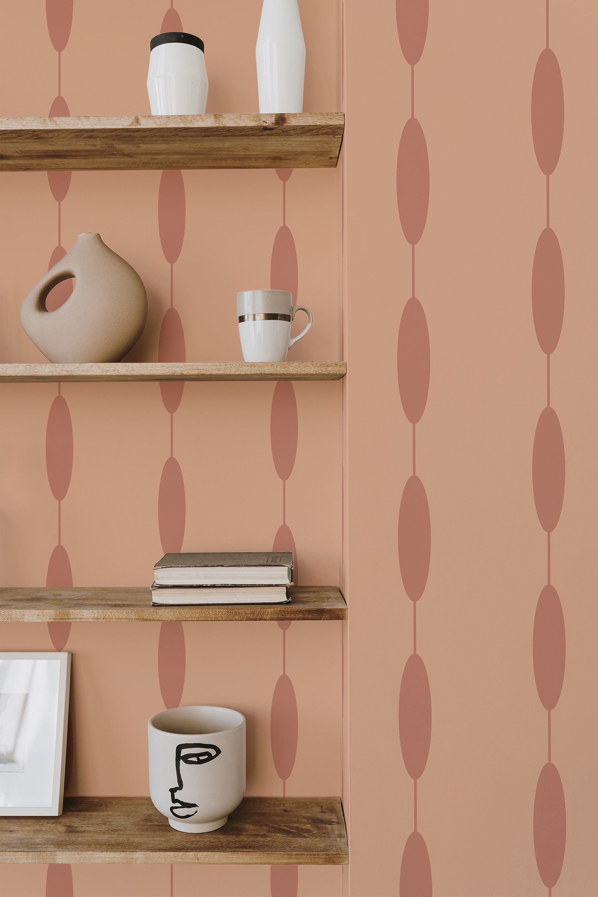 Self-adhesive wallpaper with a pattern of peach and pink ovals aligned vertically on a warm beige background, in a room with wooden shelving displaying various decorative items.