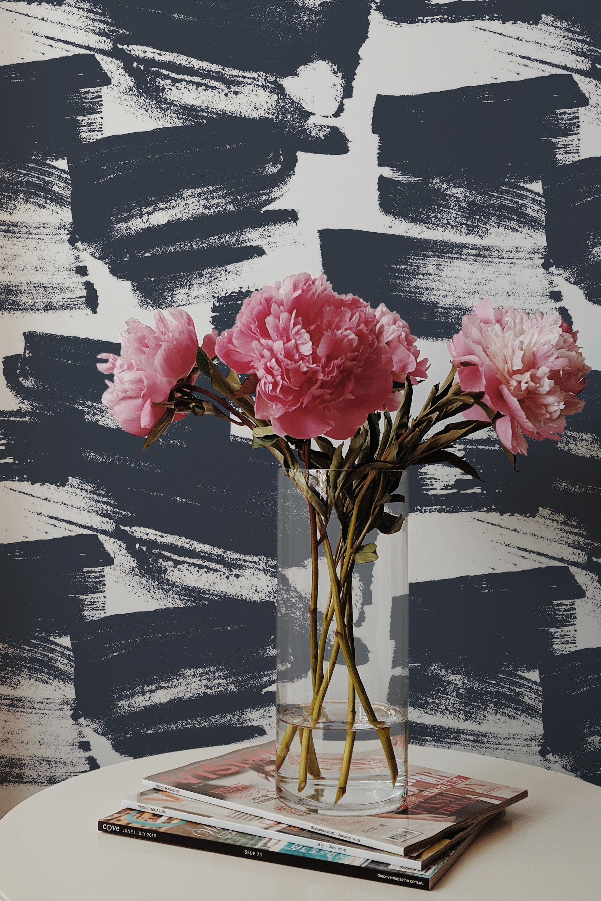 Self-adhesive wallpaper with abstract Navy Brush Strokes pattern behind a vase of pink flowers on a table.