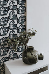 Self-adhesive monochrome brushstroke pattern wallpaper adorning a room's wall with a plant in a dark green vase on a white shelf.